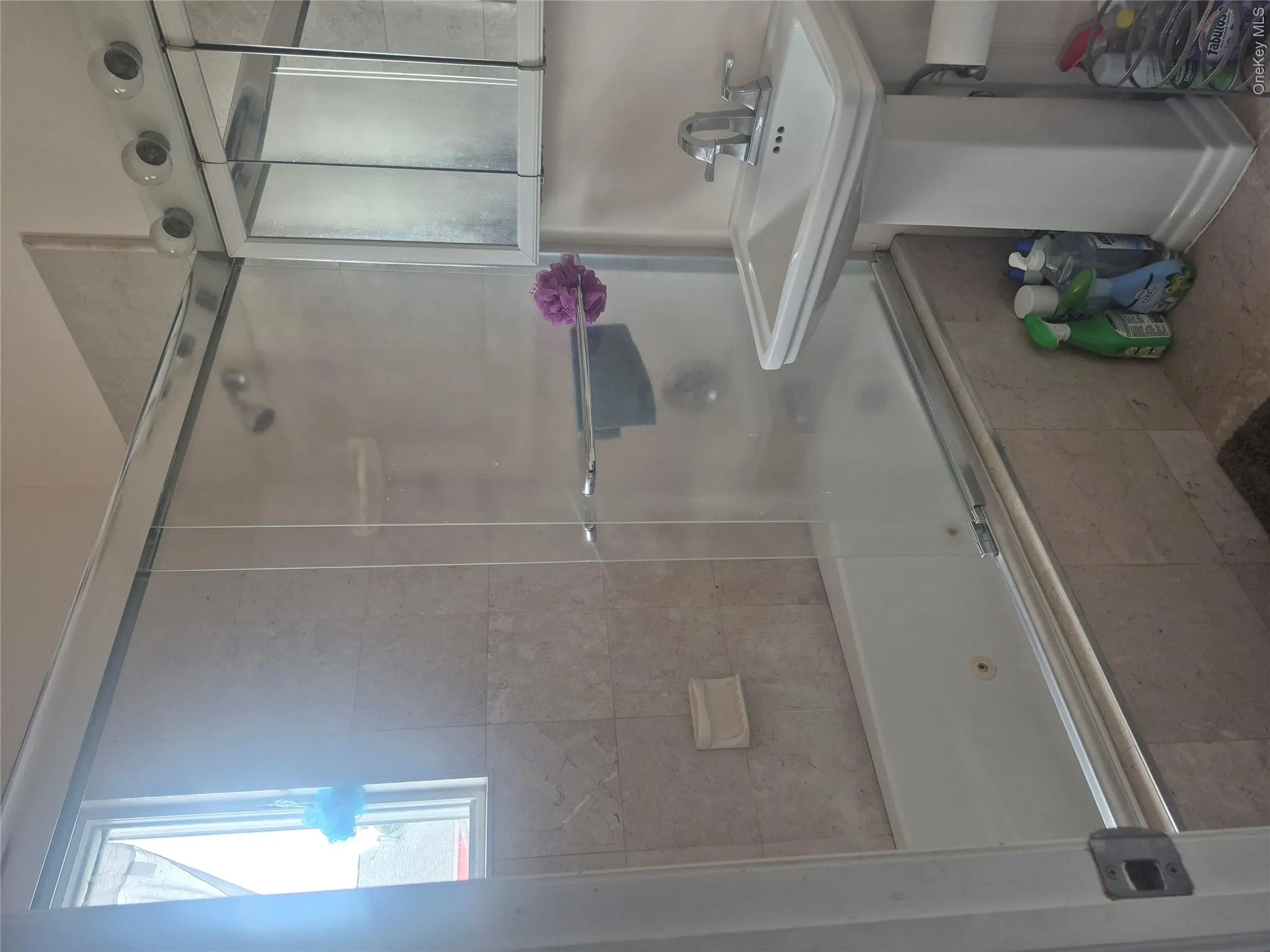 Modern bathroom featuring a frameless glass shower enclosure with chrome hardware, pedestal sink with single-handle faucet, tiled surround, and a window providing natural light Modern bathroom featuring a frameless glass shower enclosure with chrome hardware, pedestal sink with single-handle faucet, tiled surround, and a window providing natural light
