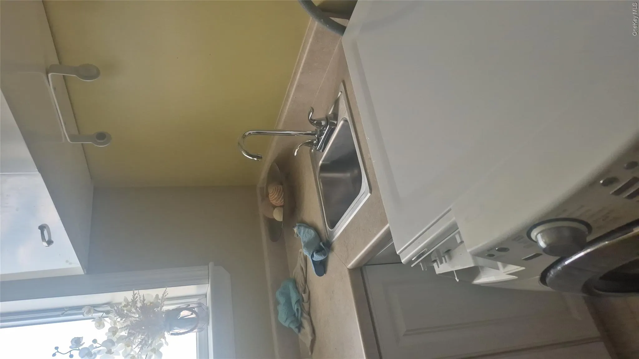 Laundry and utility area featuring a stainless steel sink, chrome faucet, and overhead cabinetry Laundry and utility area featuring a stainless steel sink, chrome faucet, and overhead cabinetry