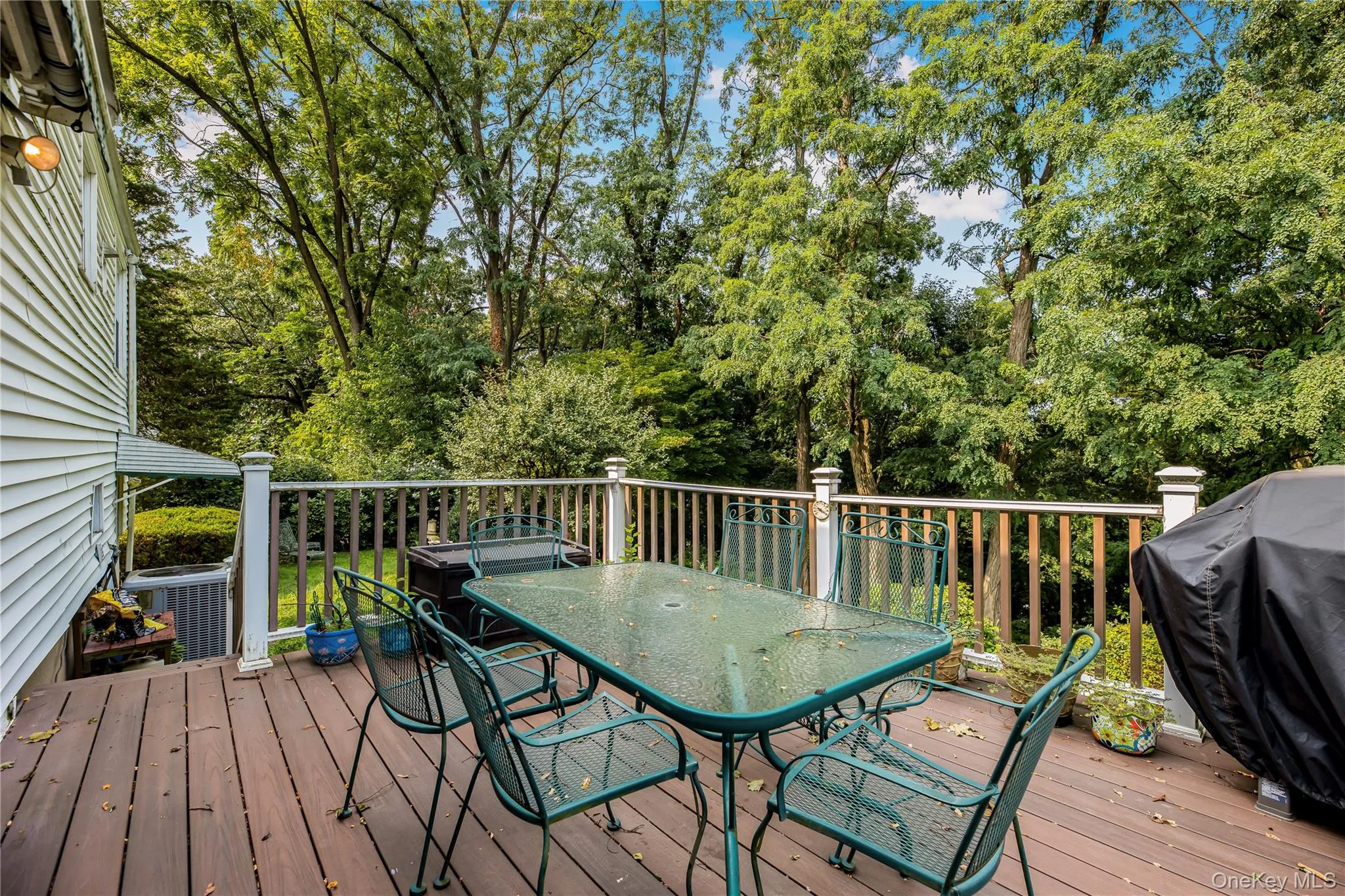 Expansive outdoor deck featuring wood-finish flooring, white railing posts, and a white siding exterior wall Expansive outdoor deck featuring wood-finish flooring, white railing posts, and a white siding exterior wall