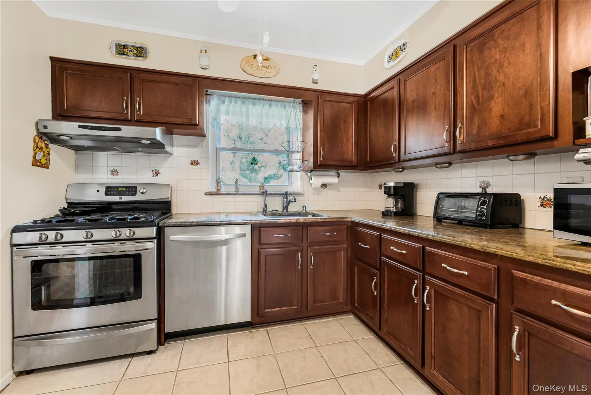 Kitchen featuring wood-finish cabinetry, stainless steel range with overhead hood, stainless steel dishwasher, tile flooring, and a tile backsplash Kitchen featuring wood-finish cabinetry, stainless steel range with overhead hood, stainless steel dishwasher, tile flooring, and a tile backsplash