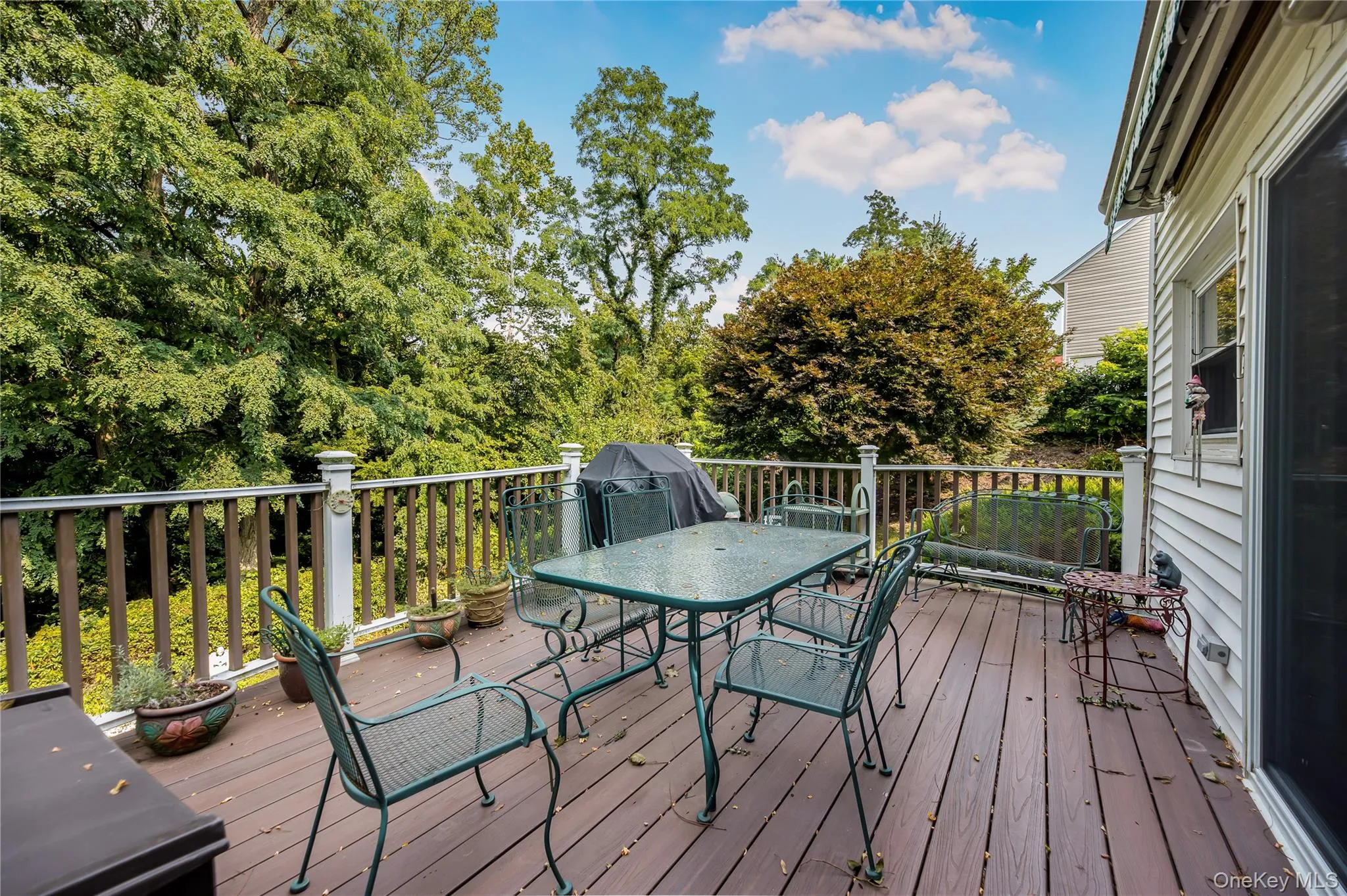 Expansive outdoor deck featuring wood-finish flooring, white railing posts, and a white siding exterior wall Expansive outdoor deck featuring wood-finish flooring, white railing posts, and a white siding exterior wall