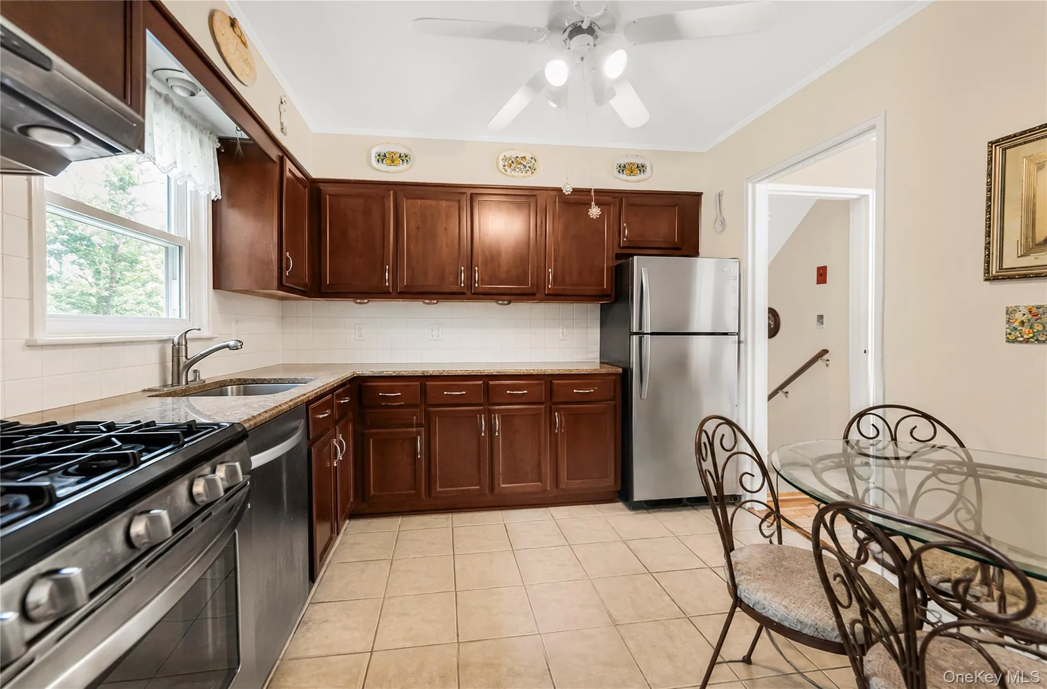 Kitchen with dark wood cabinetry, light-toned countertops, stainless steel appliances, and tile flooring Kitchen with dark wood cabinetry, light-toned countertops, stainless steel appliances, and tile flooring