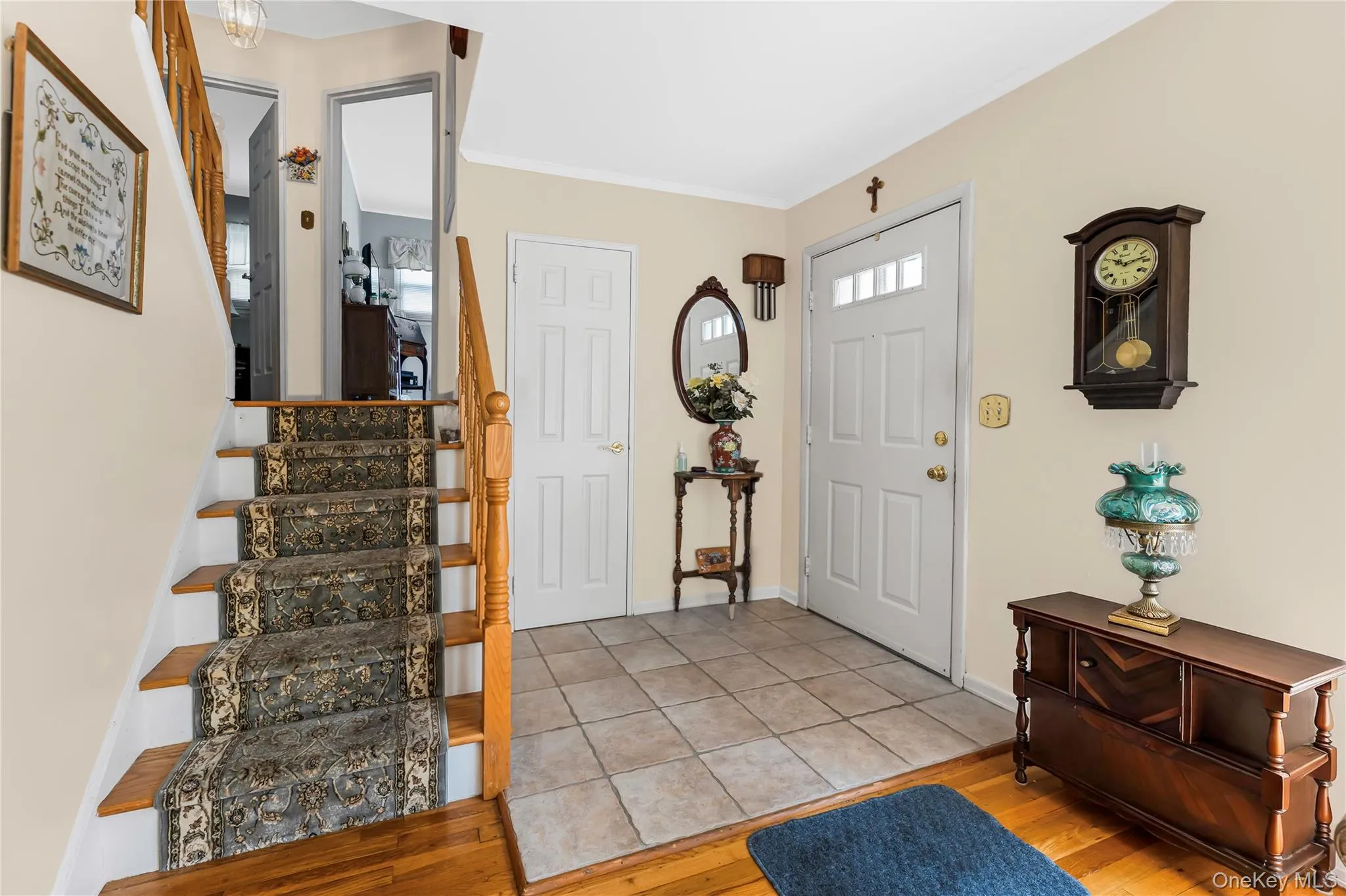 Entryway featuring wood-finish flooring, tile flooring, a staircase with wood railing, and a white paneled entry door with transom windows Entryway featuring wood-finish flooring, tile flooring, a staircase with wood railing, and a white paneled entry door with transom windows