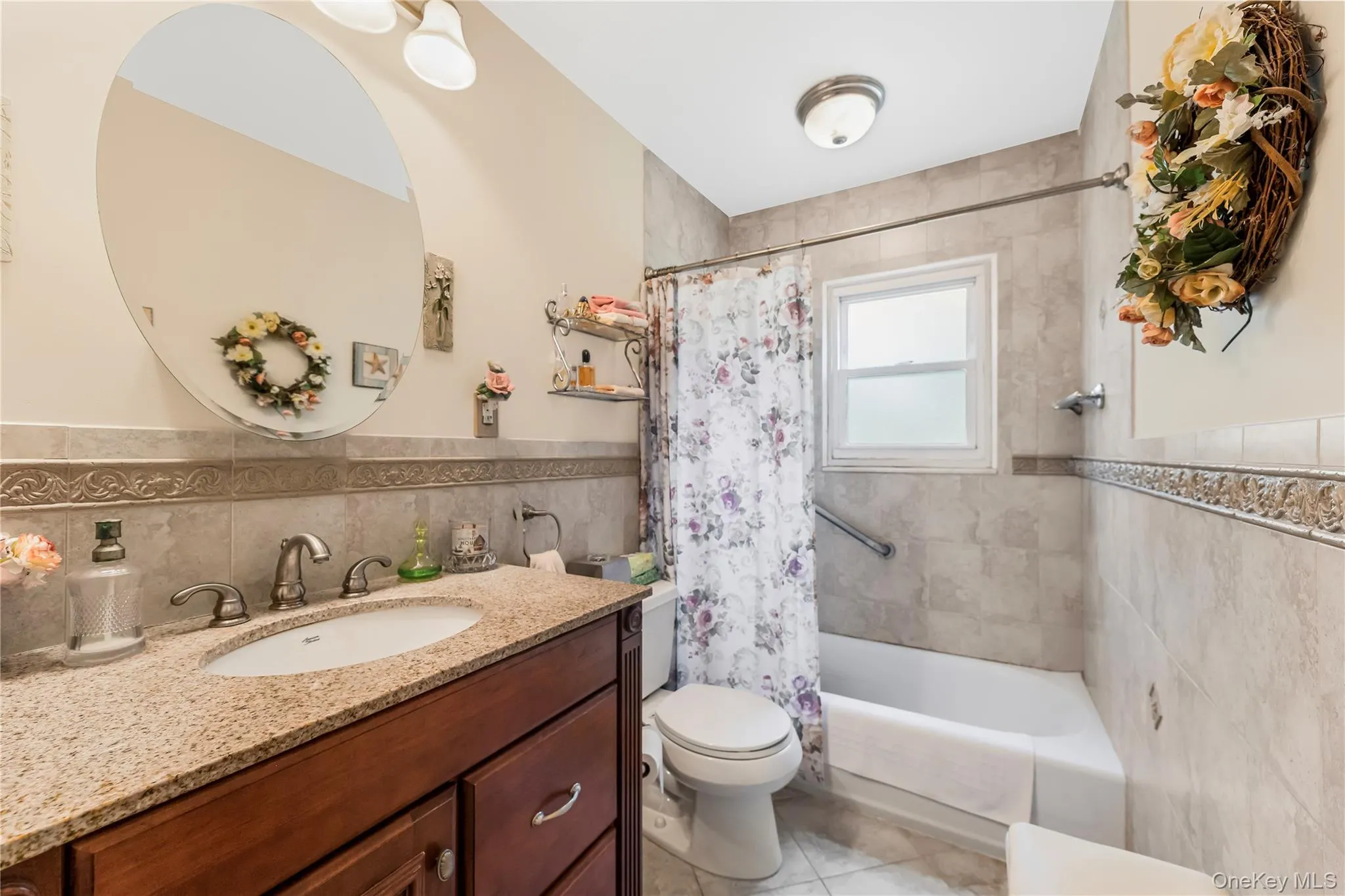 Bathroom featuring a vanity with a granite countertop, a circular mirror, a built-in tub, and wall-mounted tile Bathroom featuring a vanity with a granite countertop, a circular mirror, a built-in tub, and wall-mounted tile