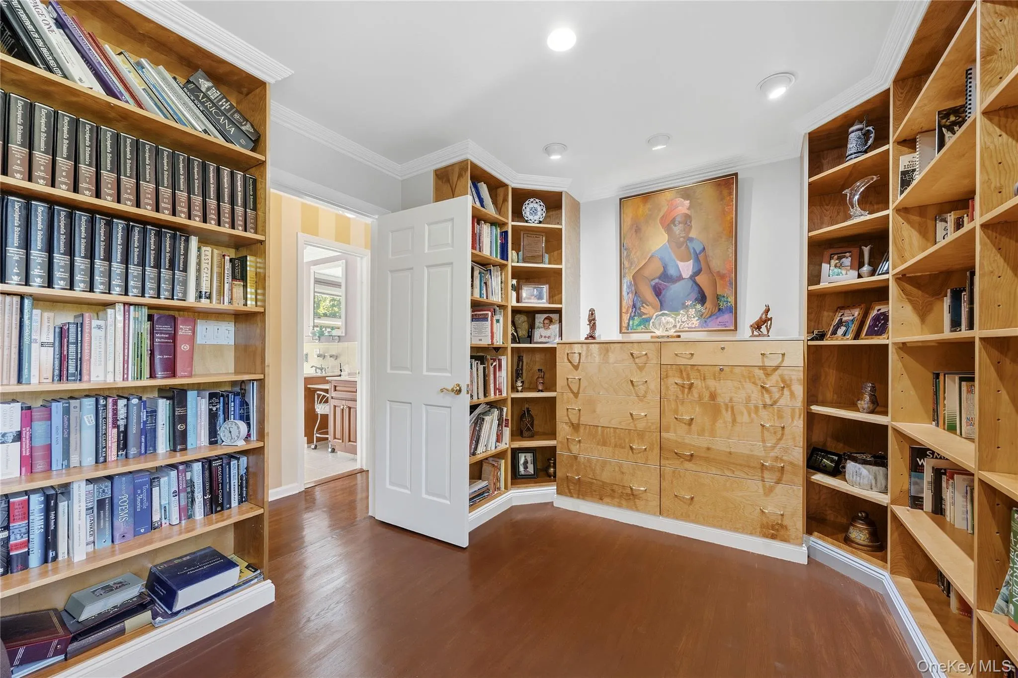 The Home Office/Library in the hallway to the first floor alternative primary suite, offers custom built-in bookshelves and 2 sets of custom drawers. Hardwood floors and recessed lights make it easy to use on day one. The Home Office/Library in the hallway to the first floor alternative primary suite, offers custom built-in bookshelves and 2 sets of custom drawers. Hardwood floors and recessed lights make it easy to use on day one.