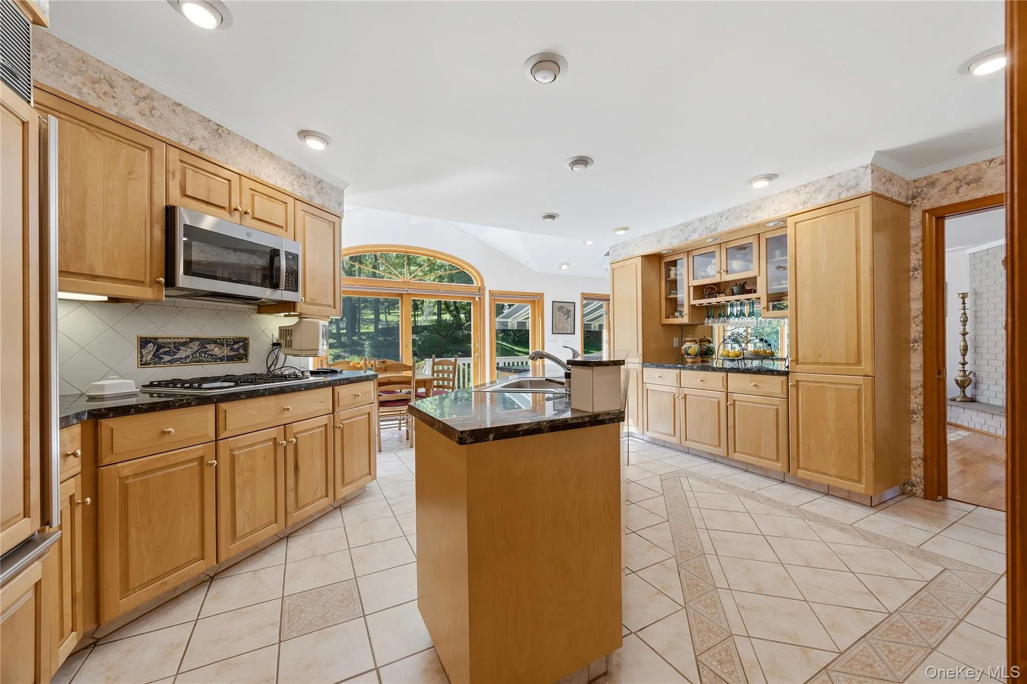 Bright Eat-In-Kitchen with inlay tile floor, marble countertops, maple cabinets, pantry closet, partial vaulted ceiling with two skylights, built-in wine rack and wine glass rack, center sink island with storage underneath, SubZero Refrigerator, Young 4-burner gas stovetop with decorative accent fish tiles above, Young GE built-in Microwave, KitchenAid Dishwasher, Young GE Double Wall Ovens, and a Breakfast Area with sliding glass door to deck with transom window Bright Eat-In-Kitchen with inlay tile floor, marble countertops, maple cabinets, pantry closet, partial vaulted ceiling with two skylights, built-in wine rack and wine glass rack, center sink island with storage underneath, SubZero Refrigerator, Young 4-burner gas stovetop with decorative accent fish tiles above, Young GE built-in Microwave, KitchenAid Dishwasher, Young GE Double Wall Ovens, and a Breakfast Area with sliding glass door to deck with transom window