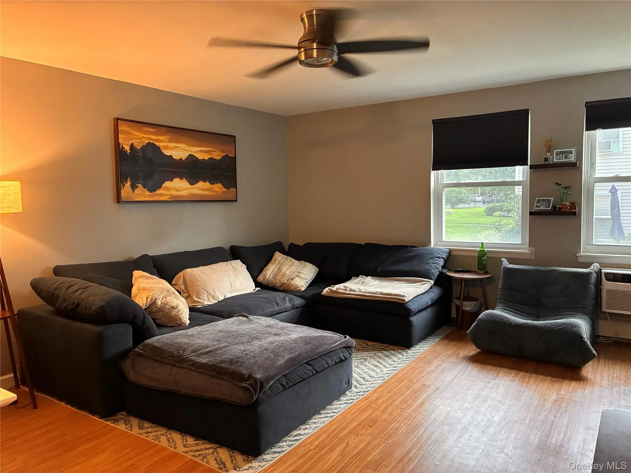 Living area featuring laminate flooring, two large windows with shades, and seating Living area featuring laminate flooring, two large windows with shades, and seating