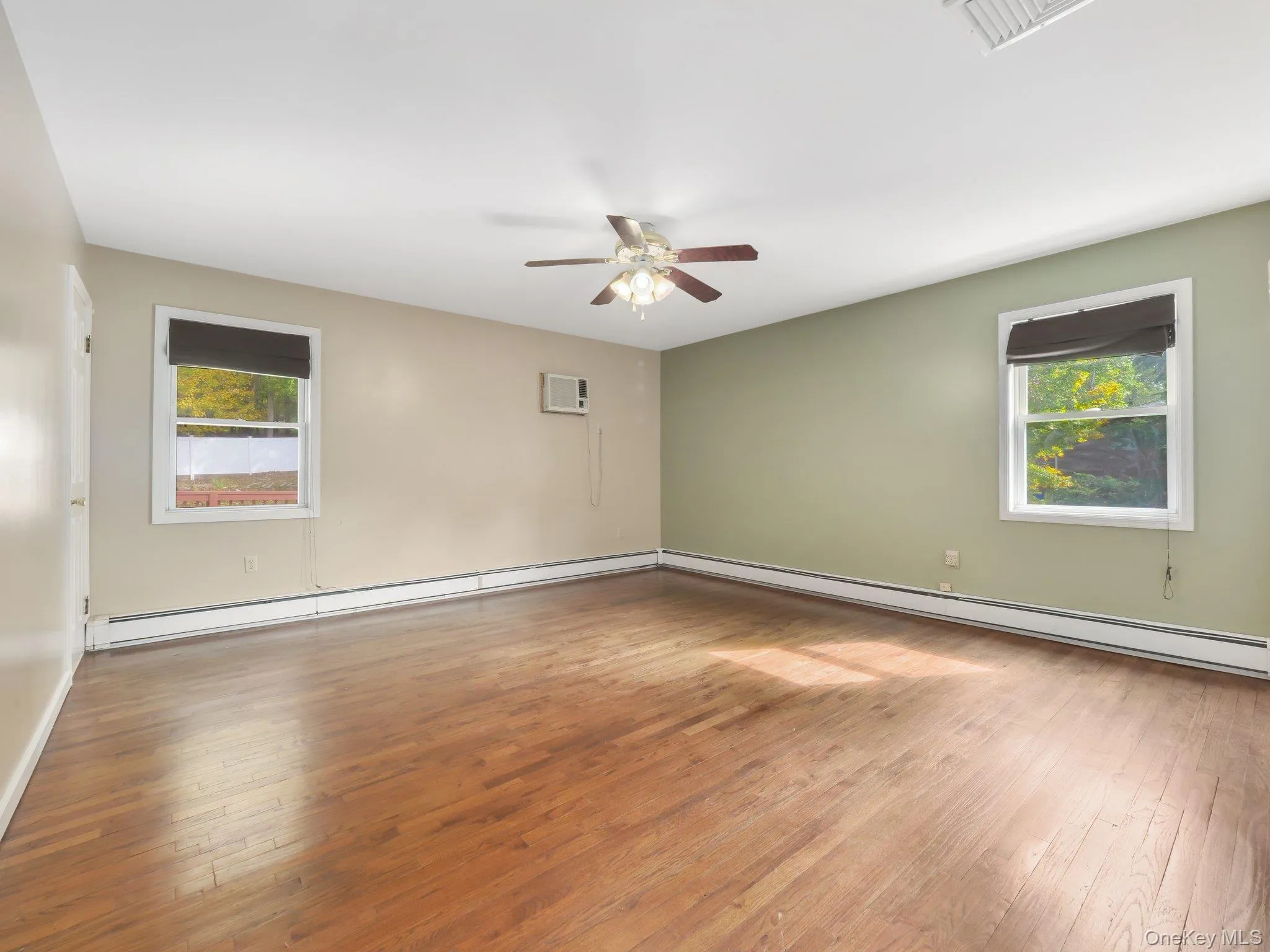 Hardwood flooring, ceiling fan, window-mounted air conditioning unit, and multiple windows with roller shades Hardwood flooring, ceiling fan, window-mounted air conditioning unit, and multiple windows with roller shades