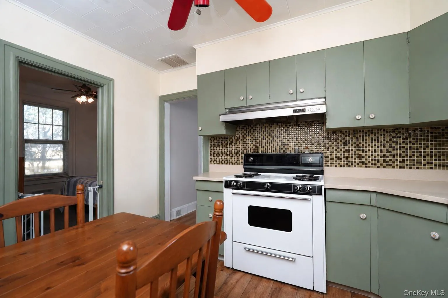 Sage green cabinetry with polished nickel hardware anchors this kitchen, featuring stainless steel appliances, a mosaic tile backsplash, and ample counter space Sage green cabinetry with polished nickel hardware anchors this kitchen, featuring stainless steel appliances, a mosaic tile backsplash, and ample counter space