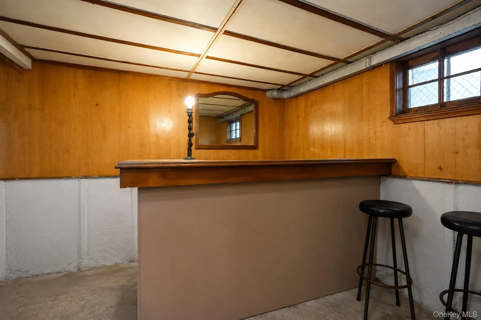 Finished basement space featuring a built-in bar with a wood-finish countertop, wood paneling, and a transom window Finished basement space featuring a built-in bar with a wood-finish countertop, wood paneling, and a transom window