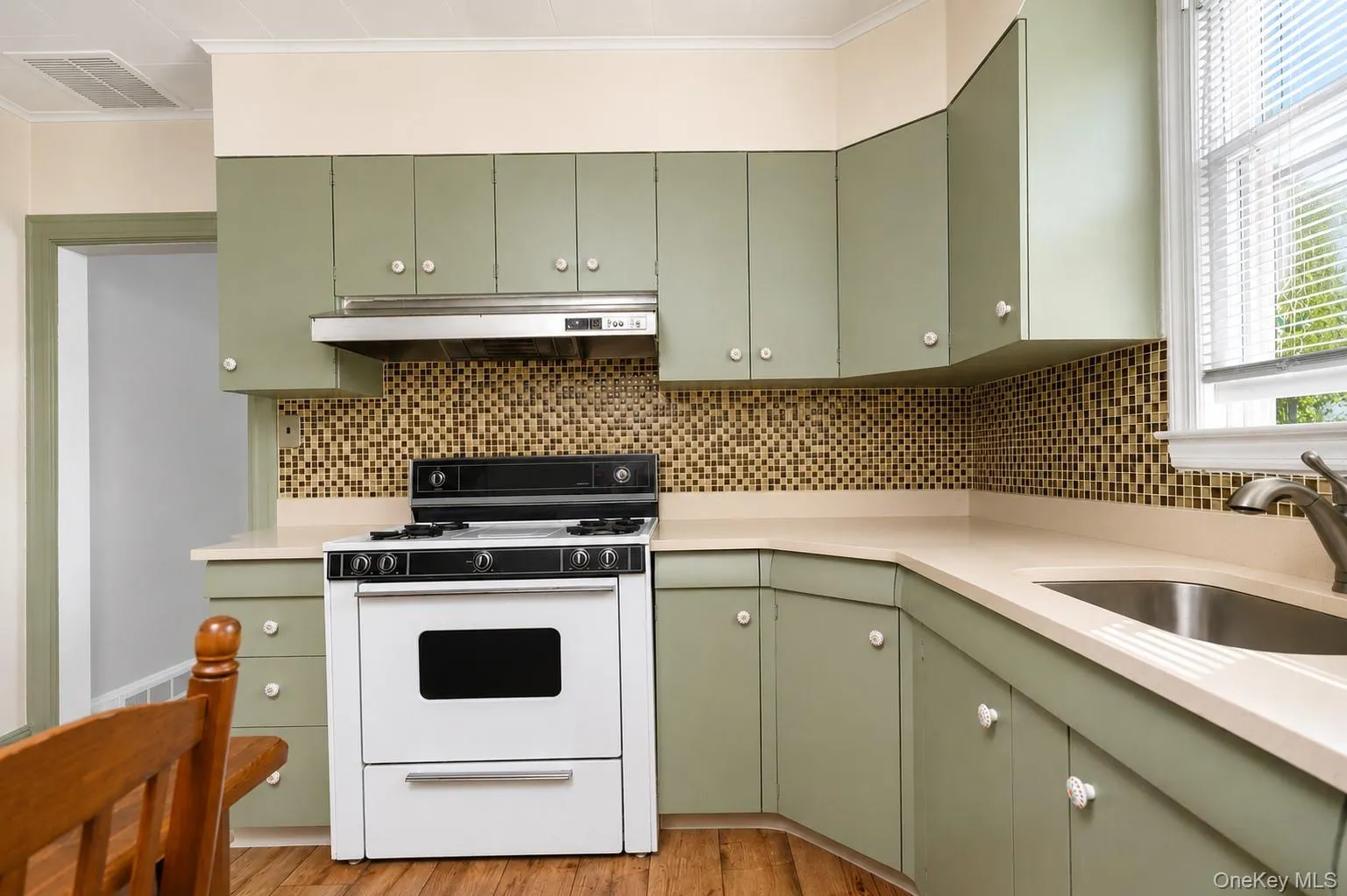 Kitchen featuring green cabinetry, tile backsplash, white countertops, and wood-finish flooring Kitchen featuring green cabinetry, tile backsplash, white countertops, and wood-finish flooring
