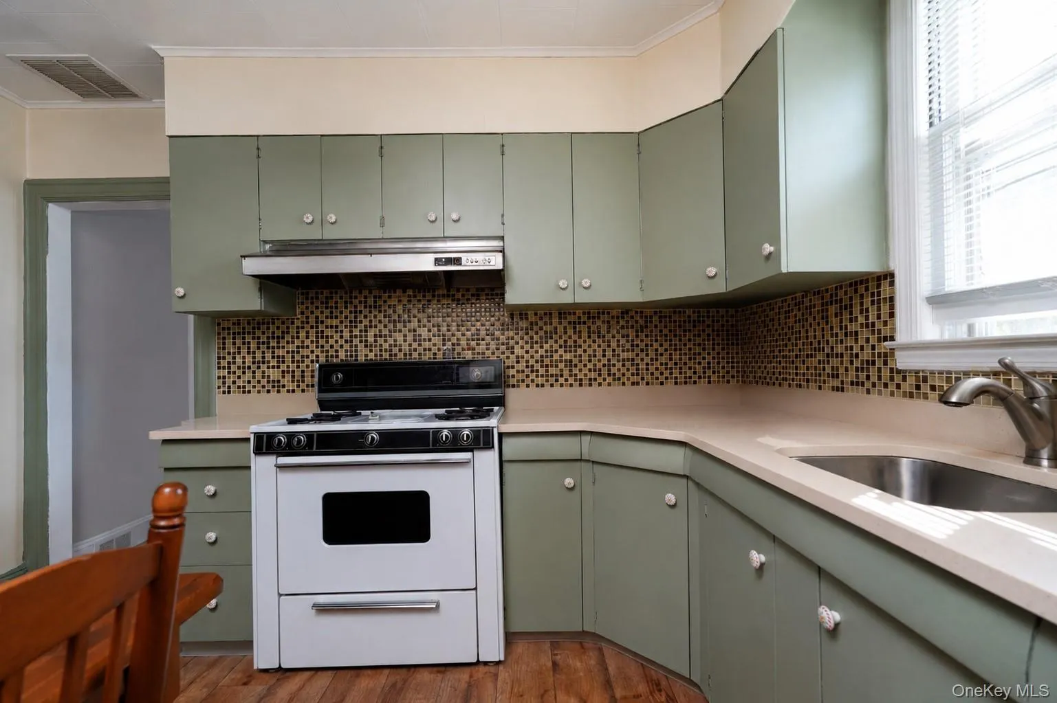 Sage-green cabinetry with polished hardware and white countertops anchors this kitchen, which features a gas range with white finish, stainless steel range hood, and a geometric tile backsplash Sage-green cabinetry with polished hardware and white countertops anchors this kitchen, which features a gas range with white finish, stainless steel range hood, and a geometric tile backsplash