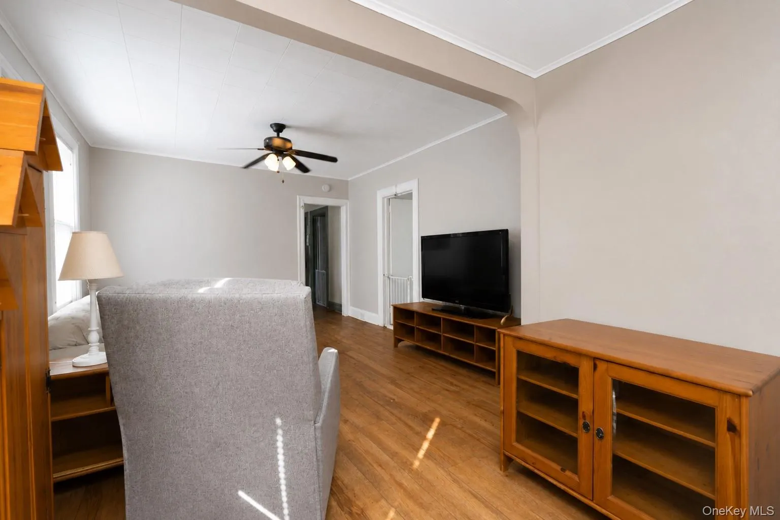 Bright living space featuring hardwood flooring, ceiling fan with integrated lighting, and built-in wood cabinetry with glass-front doors Bright living space featuring hardwood flooring, ceiling fan with integrated lighting, and built-in wood cabinetry with glass-front doors