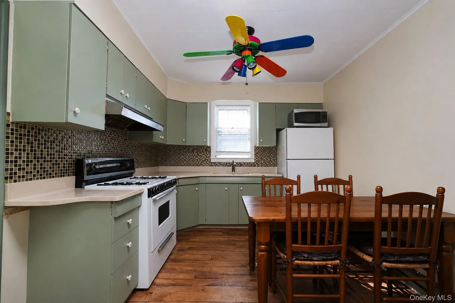 Eat-in kitchen featuring sage green cabinetry, mosaic tile backsplash, white electric range, and wood-finish flooring Eat-in kitchen featuring sage green cabinetry, mosaic tile backsplash, white electric range, and wood-finish flooring