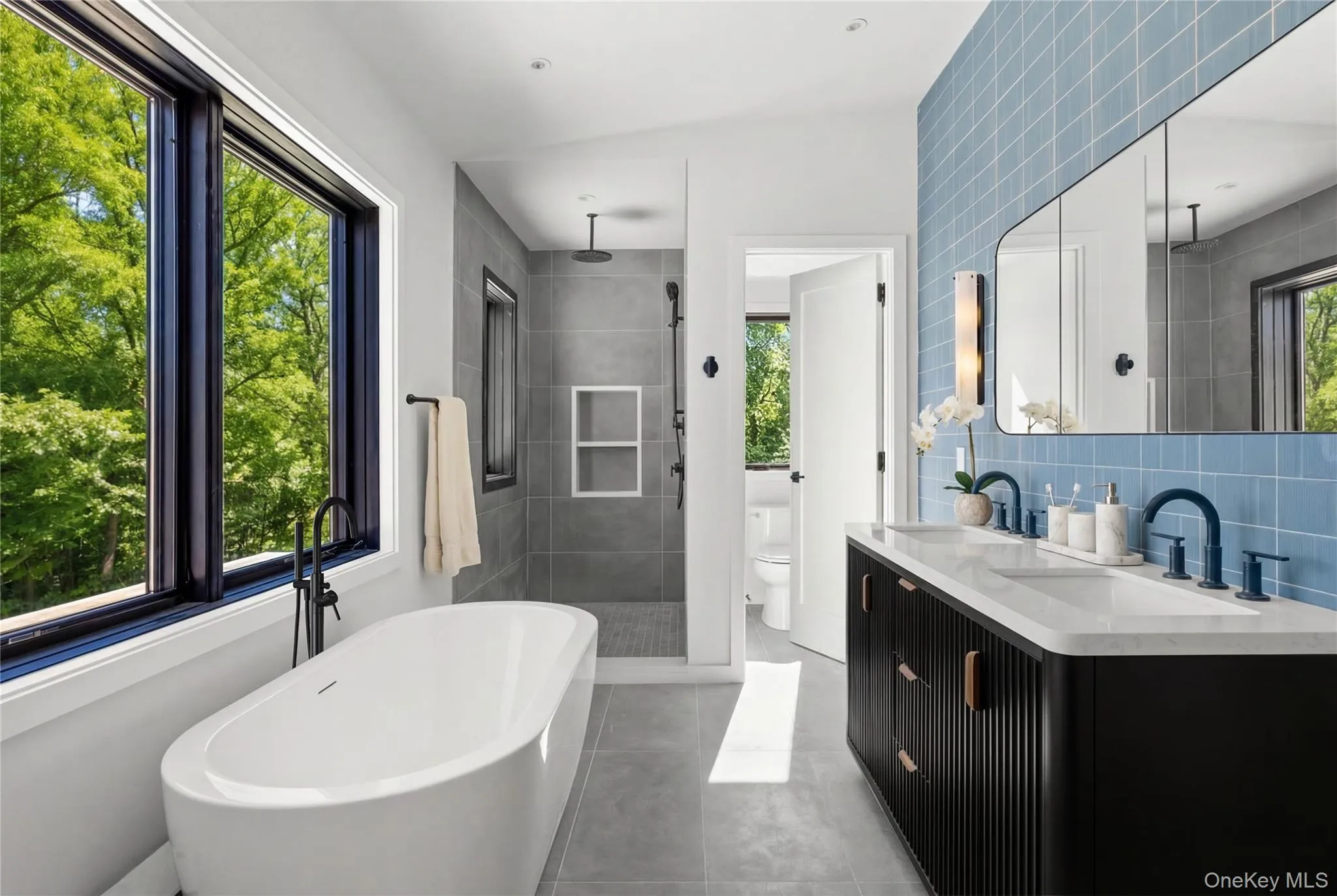 Freestanding soaking tub, large black-framed windows, dual vanity with undermount sinks, geometric tiled accent wall, and a walk-in shower with a rainfall showerhead Freestanding soaking tub, large black-framed windows, dual vanity with undermount sinks, geometric tiled accent wall, and a walk-in shower with a rainfall showerhead