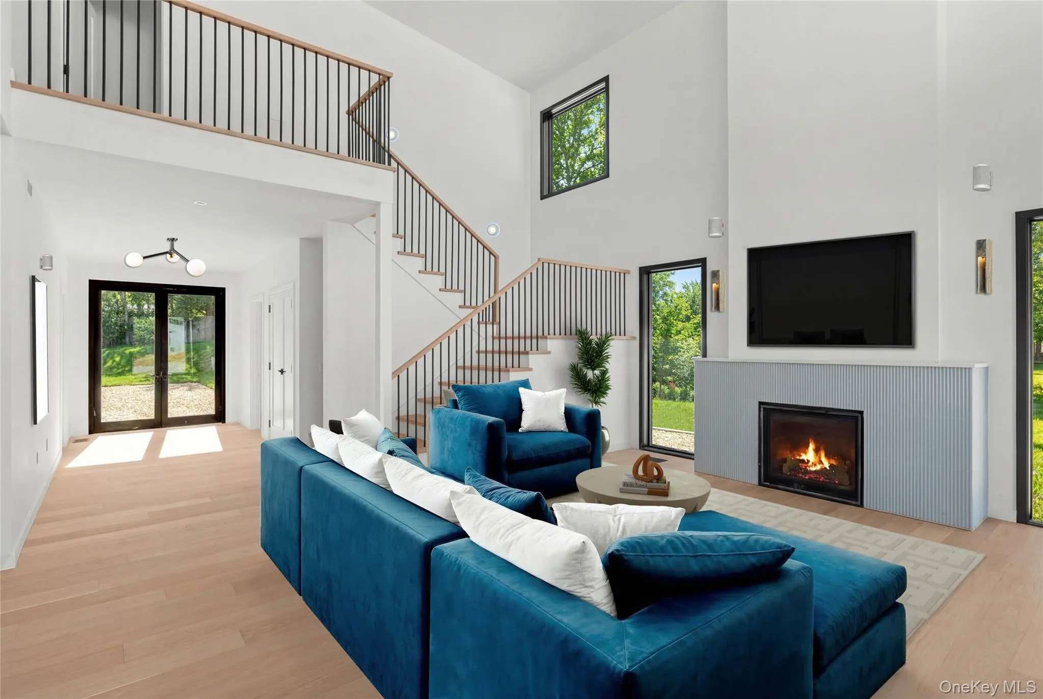 Two-story vaulted ceiling, light wood-finish flooring, two-story fireplace with a ribbed facade, open staircase with metal balusters, and multiple paneled windows Two-story vaulted ceiling, light wood-finish flooring, two-story fireplace with a ribbed facade, open staircase with metal balusters, and multiple paneled windows
