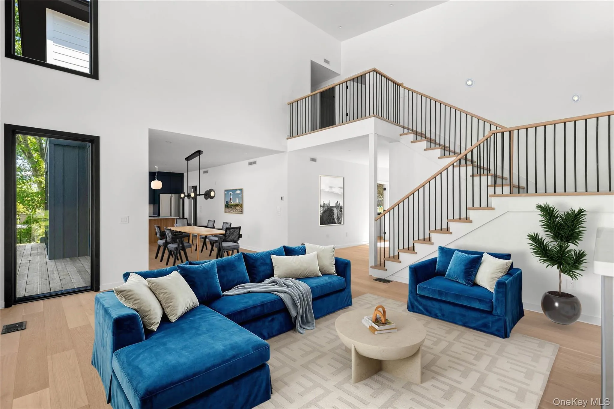 Two-story living area with high ceilings, light wood-finish flooring, and a contemporary staircase featuring wood handrails and black metal balusters Two-story living area with high ceilings, light wood-finish flooring, and a contemporary staircase featuring wood handrails and black metal balusters