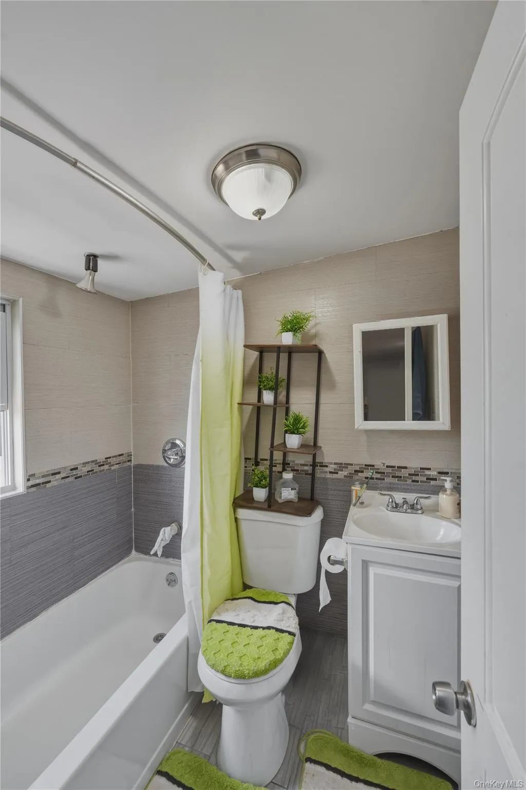 Bathroom featuring a tub with shower, white vanity with integrated sink, wall-mounted mirror cabinet, and tiled walls Bathroom featuring a tub with shower, white vanity with integrated sink, wall-mounted mirror cabinet, and tiled walls