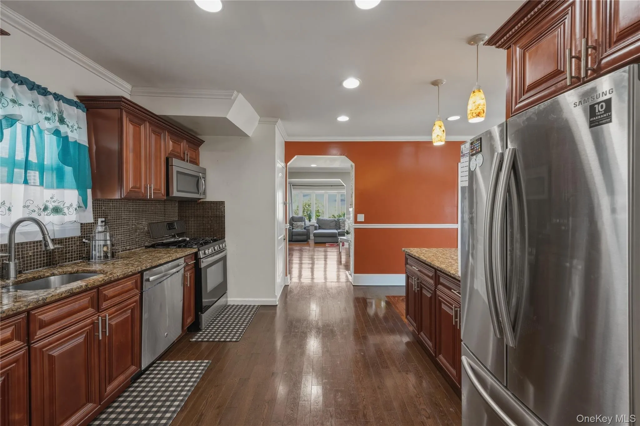 Kitchen featuring stainless steel appliances, wood-finish flooring, recessed lighting, and rich wood cabinetry with a tile backsplash Kitchen featuring stainless steel appliances, wood-finish flooring, recessed lighting, and rich wood cabinetry with a tile backsplash