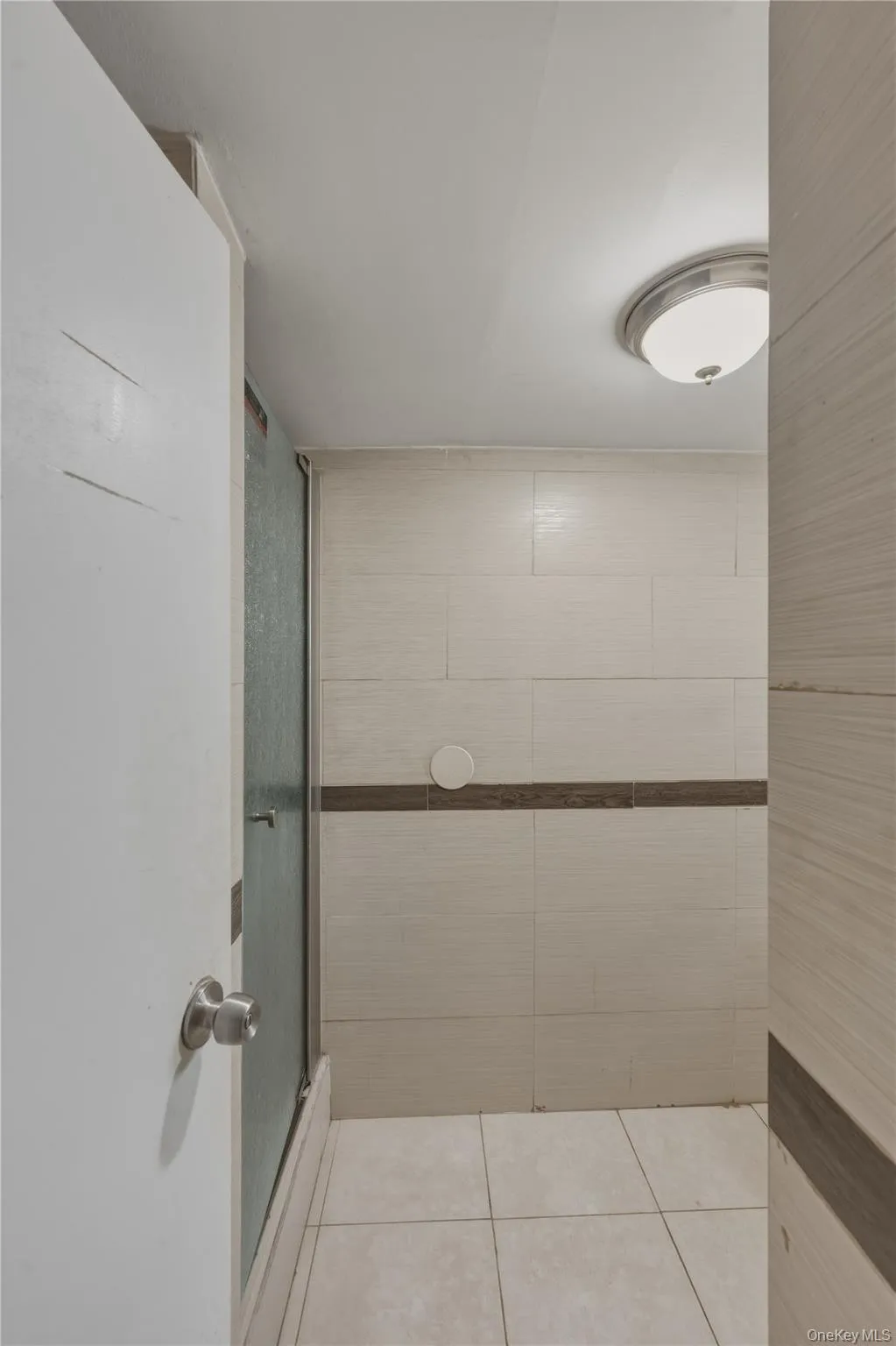 Shower enclosure with glass panel, tiled walls with a decorative accent band, and tiled flooring Shower enclosure with glass panel, tiled walls with a decorative accent band, and tiled flooring