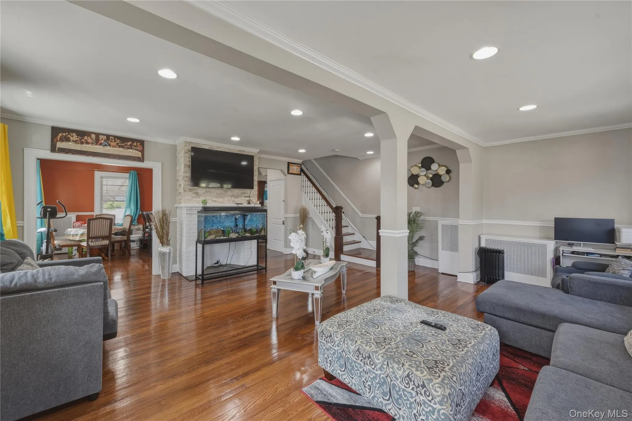 Hardwood flooring, recessed lighting, crown molding, white stacked stone fireplace surround, and a dining area with a window Hardwood flooring, recessed lighting, crown molding, white stacked stone fireplace surround, and a dining area with a window