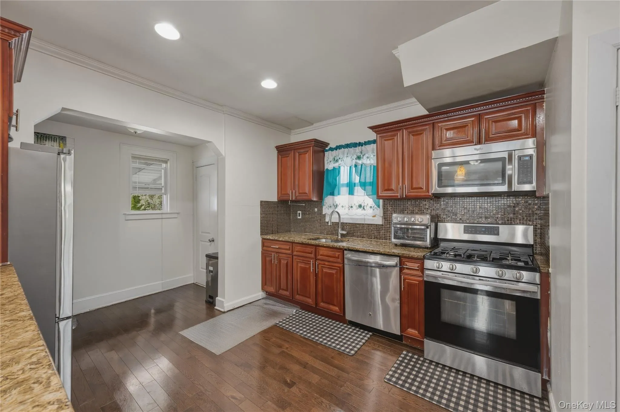 Kitchen with wood-finish flooring, recessed lighting, wood cabinetry, stone countertops, and stainless steel appliances Kitchen with wood-finish flooring, recessed lighting, wood cabinetry, stone countertops, and stainless steel appliances
