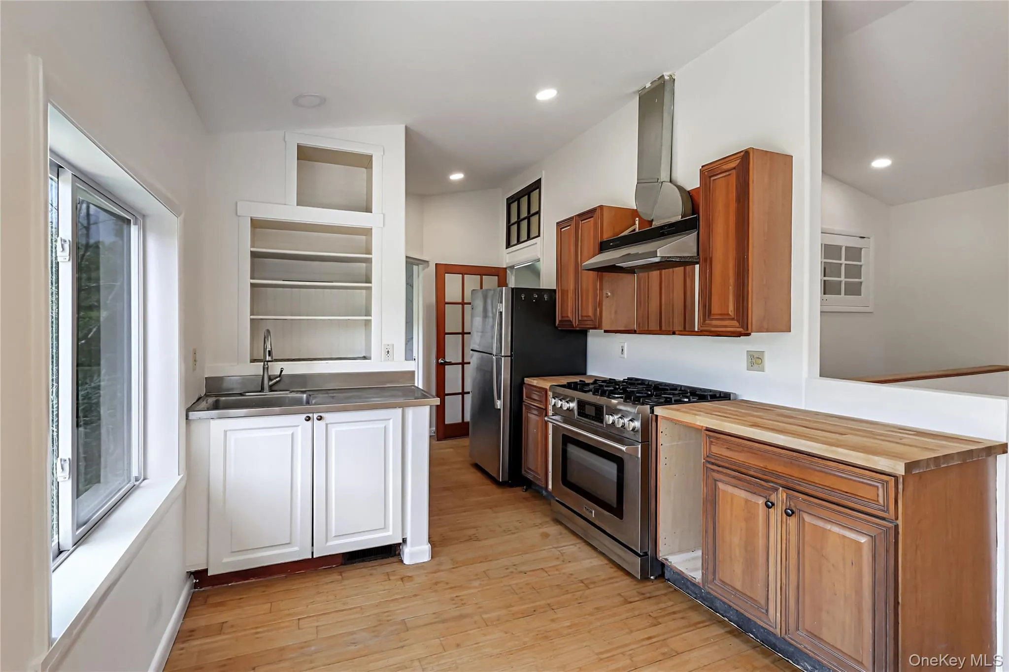 Kitchen featuring wood-finish flooring, stainless steel appliances, recessed lighting, and a stainless steel sink with open shelving Kitchen featuring wood-finish flooring, stainless steel appliances, recessed lighting, and a stainless steel sink with open shelving