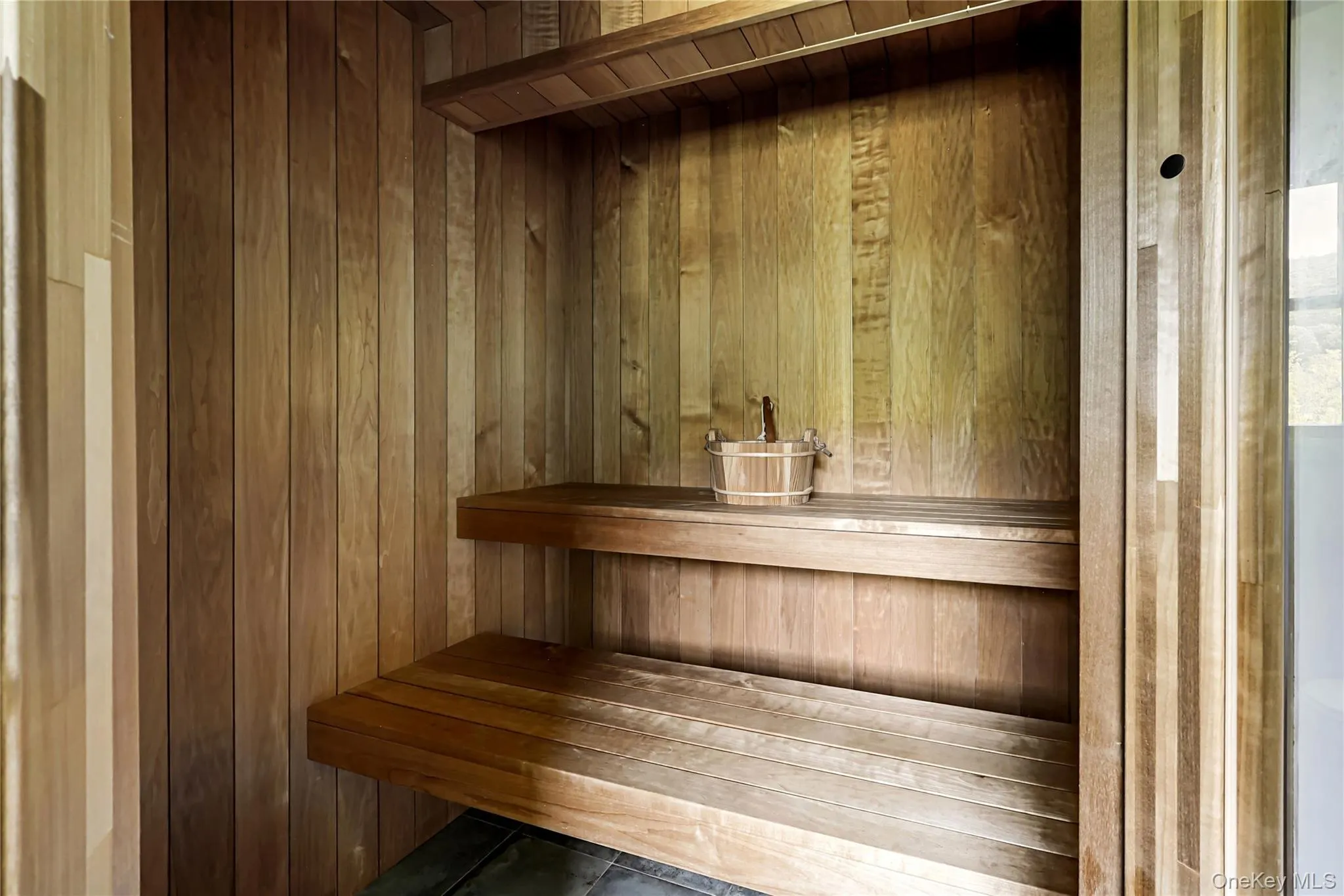 Sauna featuring wood paneling, built-in shelving, and tiered wood benches Sauna featuring wood paneling, built-in shelving, and tiered wood benches