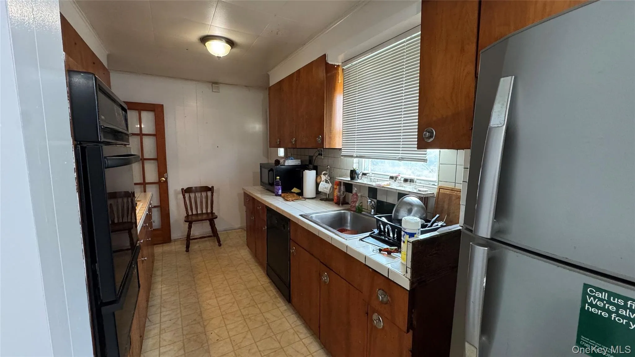 Galley kitchen featuring wood cabinetry, integrated double oven, and stainless steel refrigerator Galley kitchen featuring wood cabinetry, integrated double oven, and stainless steel refrigerator