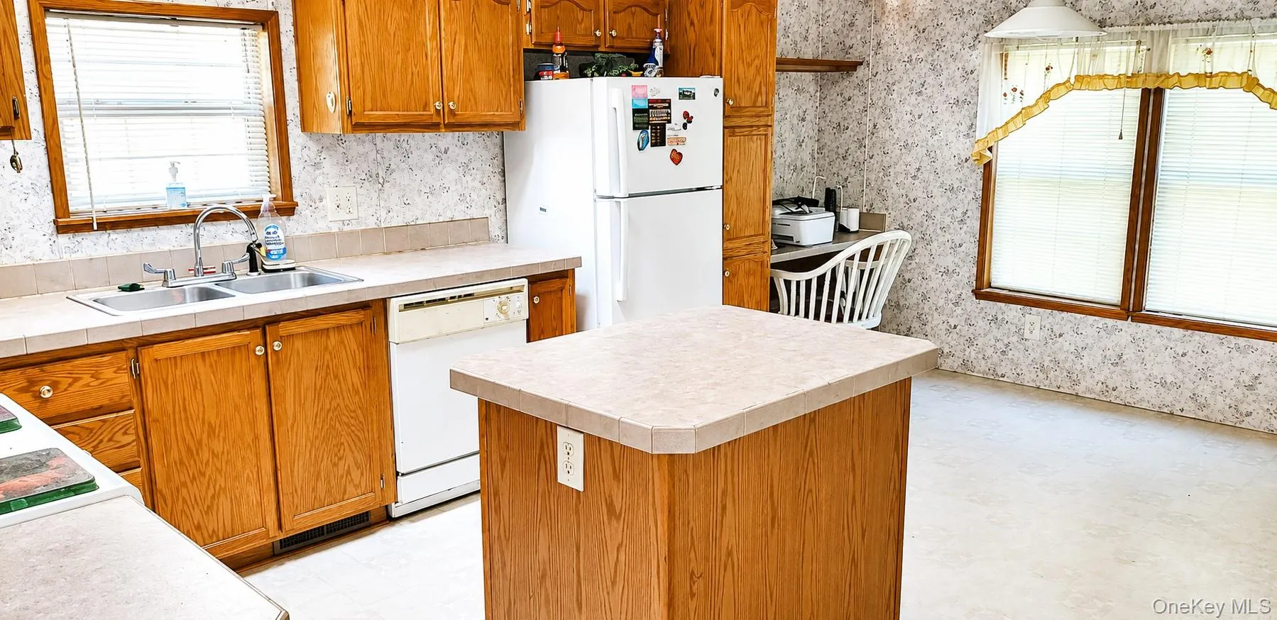 Kitchen featuring wood-finish cabinetry, a double basin stainless steel sink, built-in dishwasher, and a central island with a countertop Kitchen featuring wood-finish cabinetry, a double basin stainless steel sink, built-in dishwasher, and a central island with a countertop