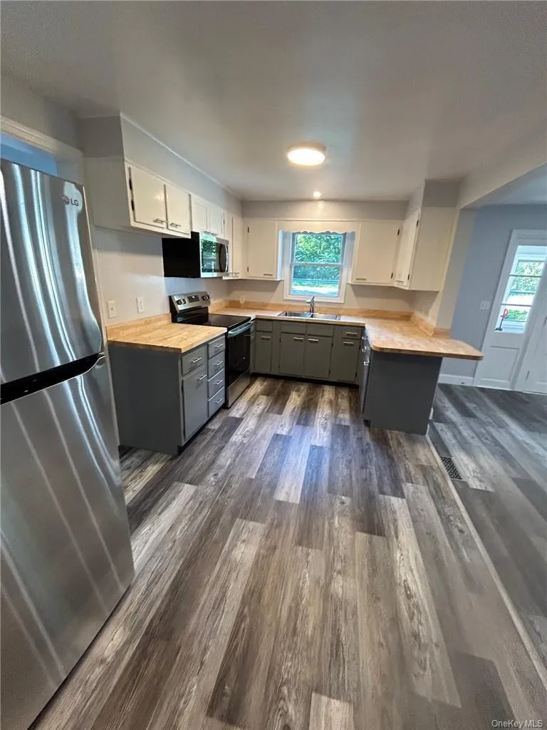Kitchen featuring abundant natural light, contemporary gray vinyl plank flooring, Acacia butcher block countertops, appliances with stainless steel finishes, and gray cabinetry Kitchen featuring abundant natural light, contemporary gray vinyl plank flooring, Acacia butcher block countertops, appliances with stainless steel finishes, and gray cabinetry
