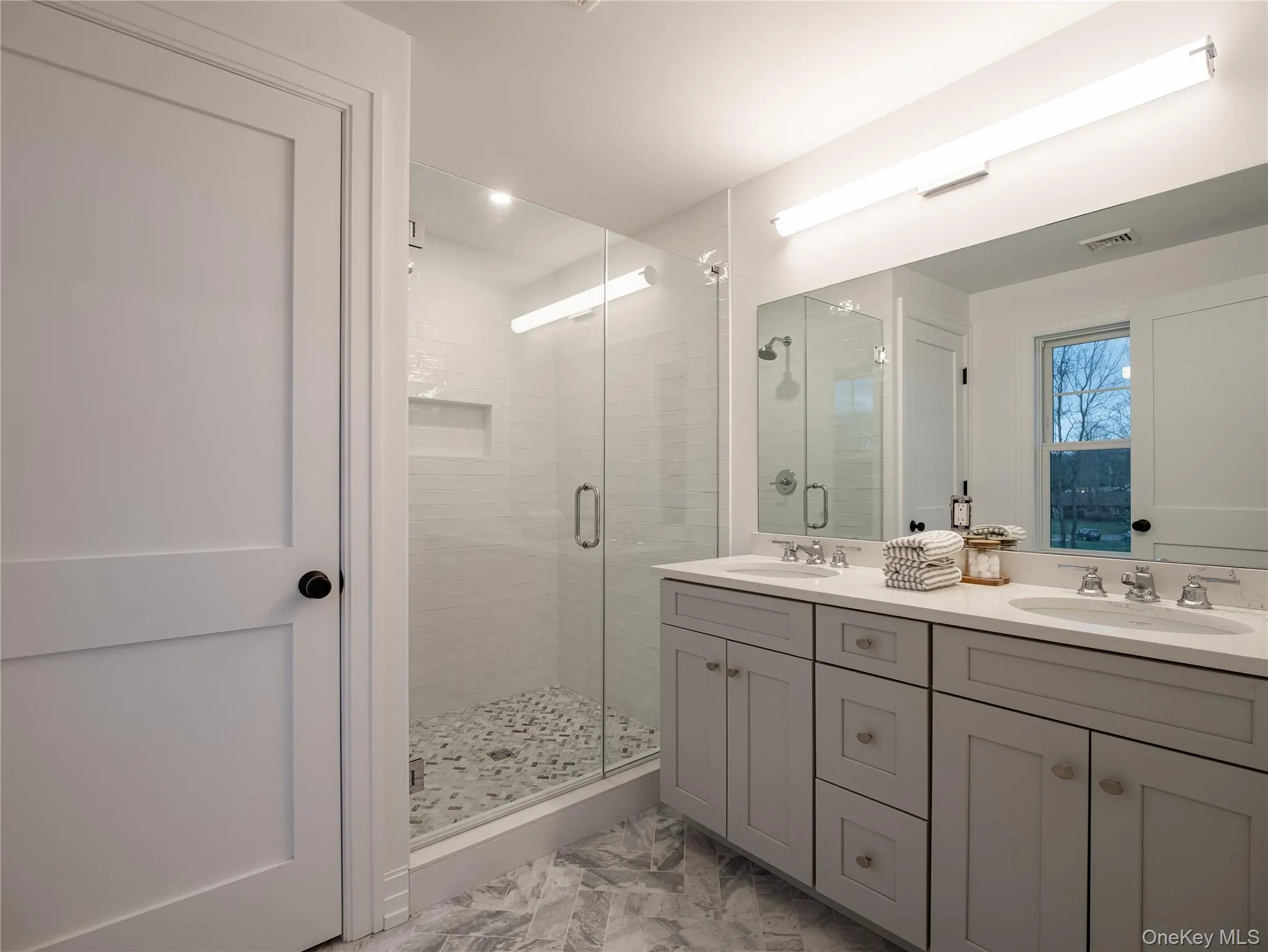 Bathroom featuring double vanity, a stall shower, and light marble finish flooring Bathroom featuring double vanity, a stall shower, and light marble finish flooring