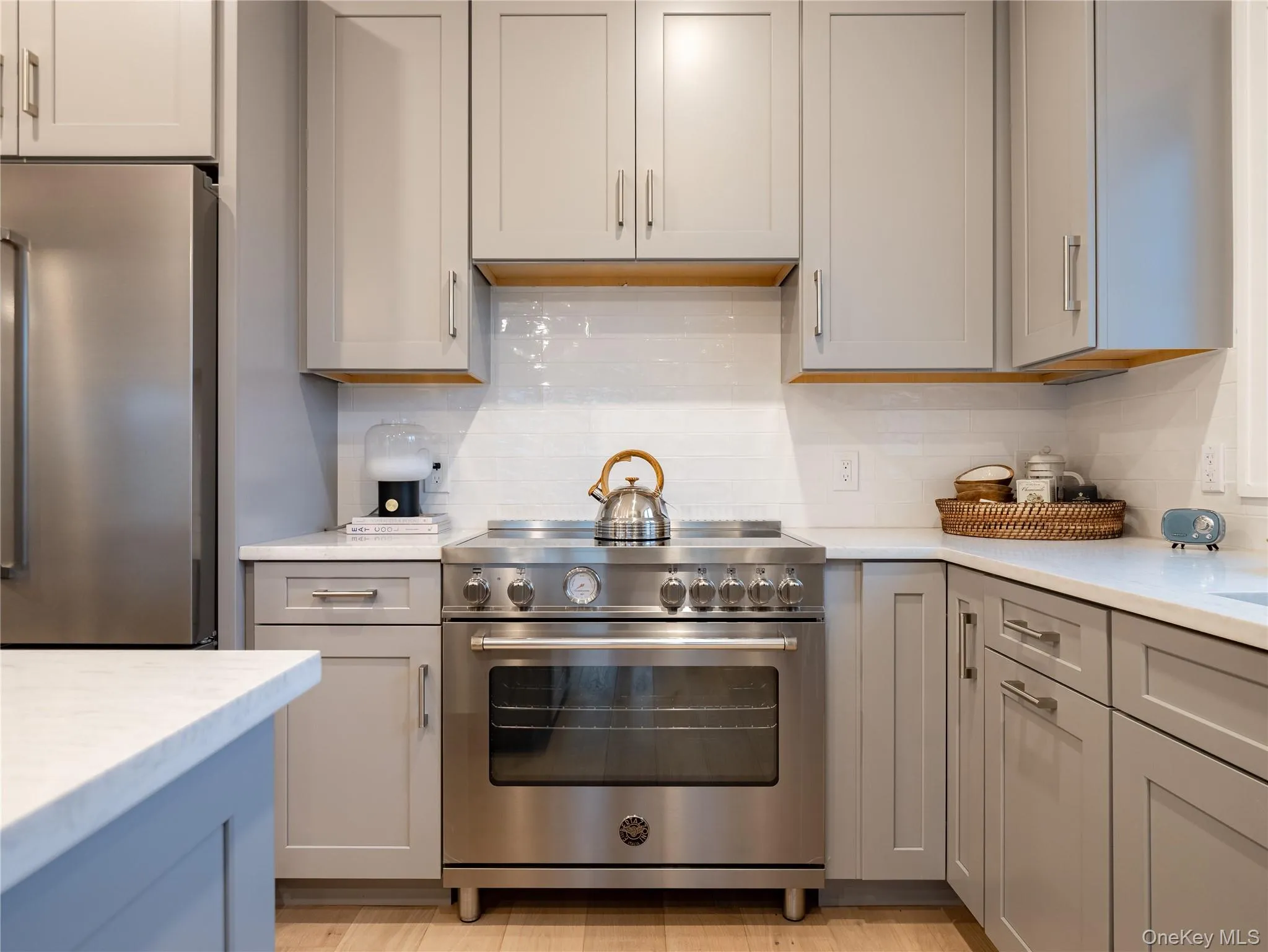 Kitchen with appliances with stainless steel finishes, gray cabinetry, backsplash, and light stone countertops Kitchen with appliances with stainless steel finishes, gray cabinetry, backsplash, and light stone countertops