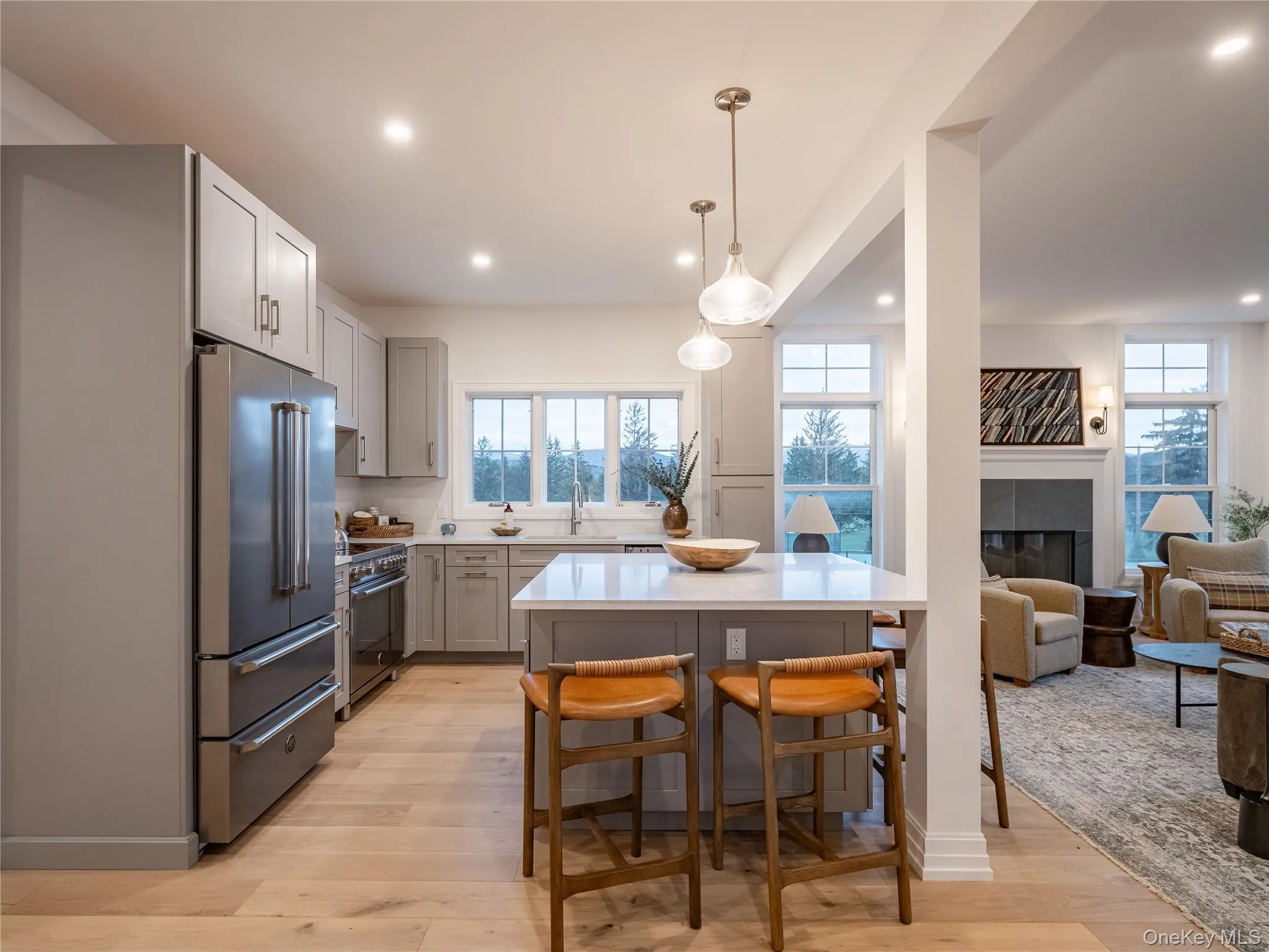 Kitchen with a tiled fireplace, high quality appliances, pendant lighting, light wood finished floors, and a kitchen breakfast bar Kitchen with a tiled fireplace, high quality appliances, pendant lighting, light wood finished floors, and a kitchen breakfast bar