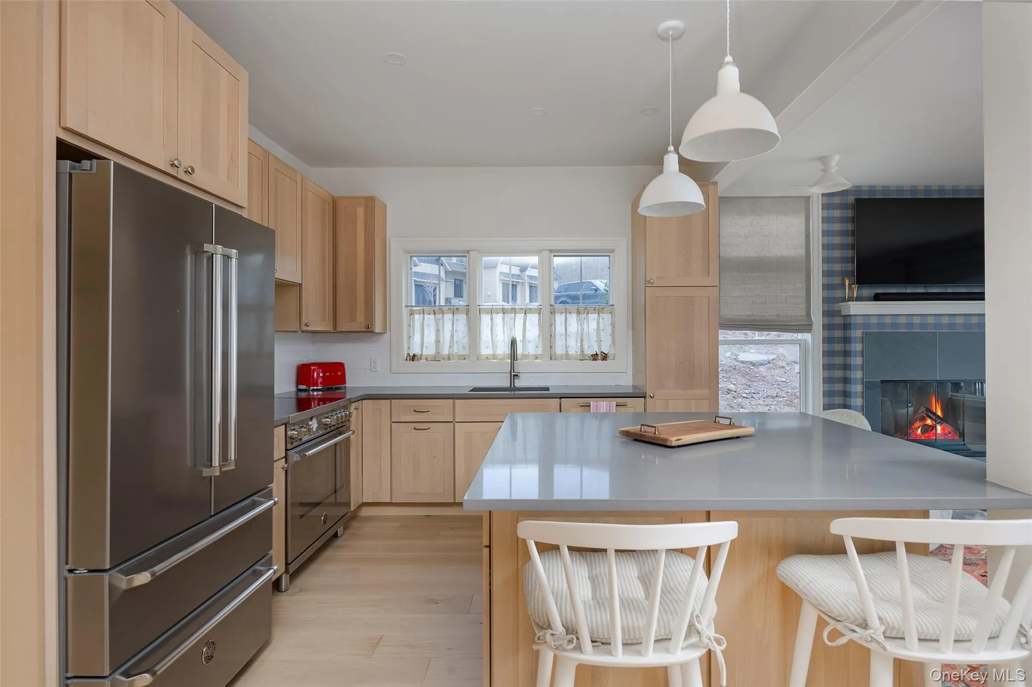 Kitchen featuring light brown cabinets, high end appliances, a tiled fireplace, pendant lighting, and a breakfast bar area Kitchen featuring light brown cabinets, high end appliances, a tiled fireplace, pendant lighting, and a breakfast bar area