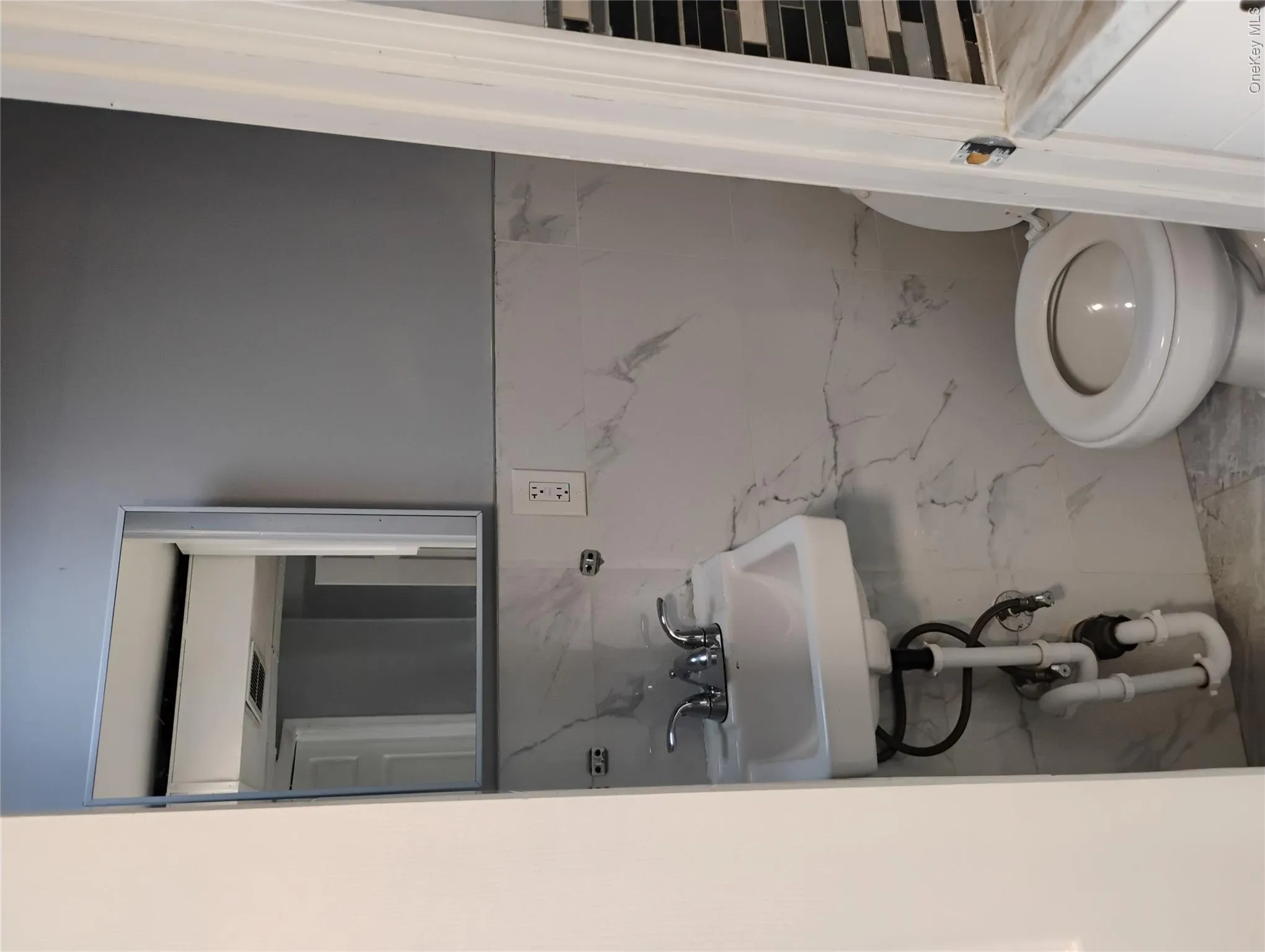 White wall-mounted sink with chrome faucet, white toilet, and tile walls White wall-mounted sink with chrome faucet, white toilet, and tile walls