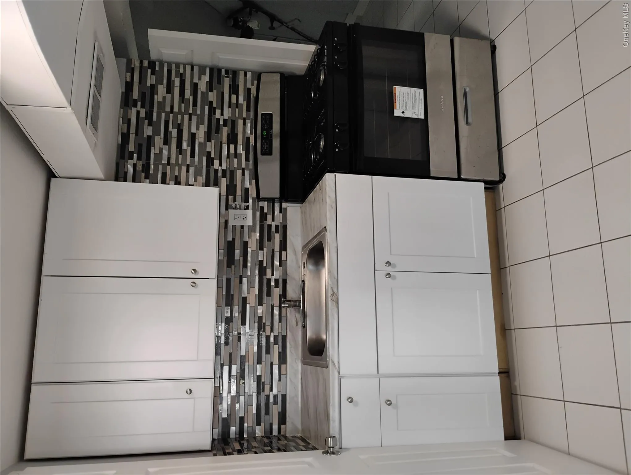 White shaker-style cabinetry, mosaic tile backsplash, stainless steel sink, stainless steel range, and tile flooring White shaker-style cabinetry, mosaic tile backsplash, stainless steel sink, stainless steel range, and tile flooring