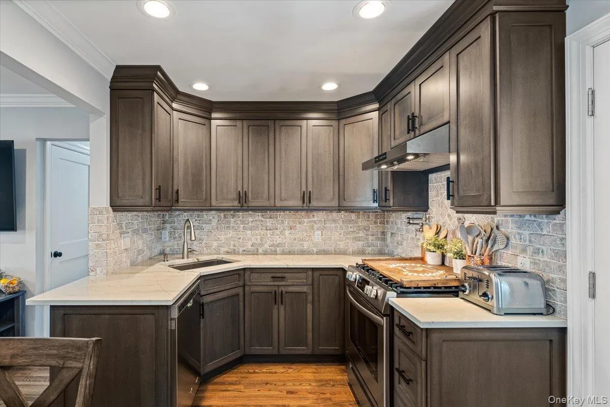Custom cabinetry with crown molding, light-toned countertops, subway tile backsplash, stainless steel appliances, and recessed lighting Custom cabinetry with crown molding, light-toned countertops, subway tile backsplash, stainless steel appliances, and recessed lighting