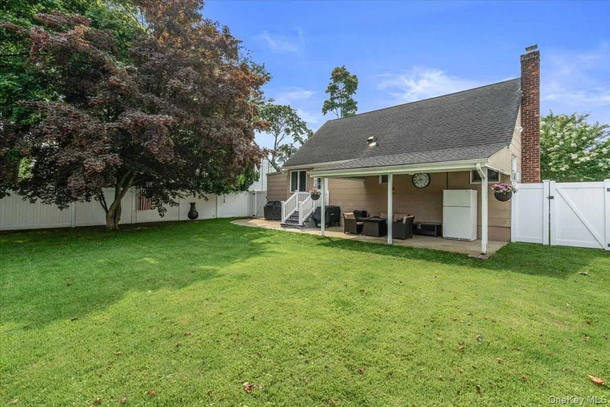 Expansive backyard featuring a covered patio, manicured lawn, mature trees, and a white privacy fence Expansive backyard featuring a covered patio, manicured lawn, mature trees, and a white privacy fence