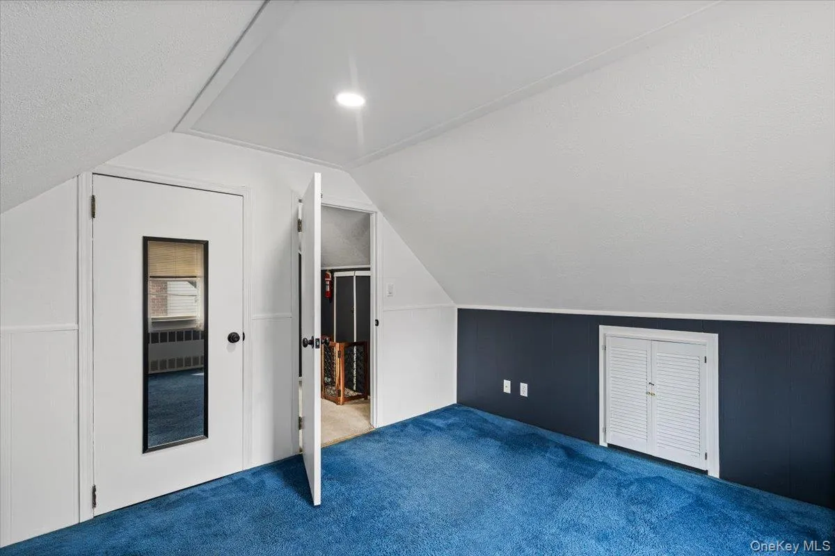 Finished attic space featuring sloped ceilings, recessed lighting, and blue carpeting throughout Finished attic space featuring sloped ceilings, recessed lighting, and blue carpeting throughout