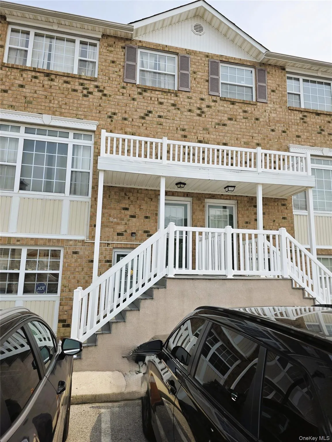 Brick exterior with white trim, featuring a prominent entryway balcony, white railing staircase, and multiple windows with white frames Brick exterior with white trim, featuring a prominent entryway balcony, white railing staircase, and multiple windows with white frames