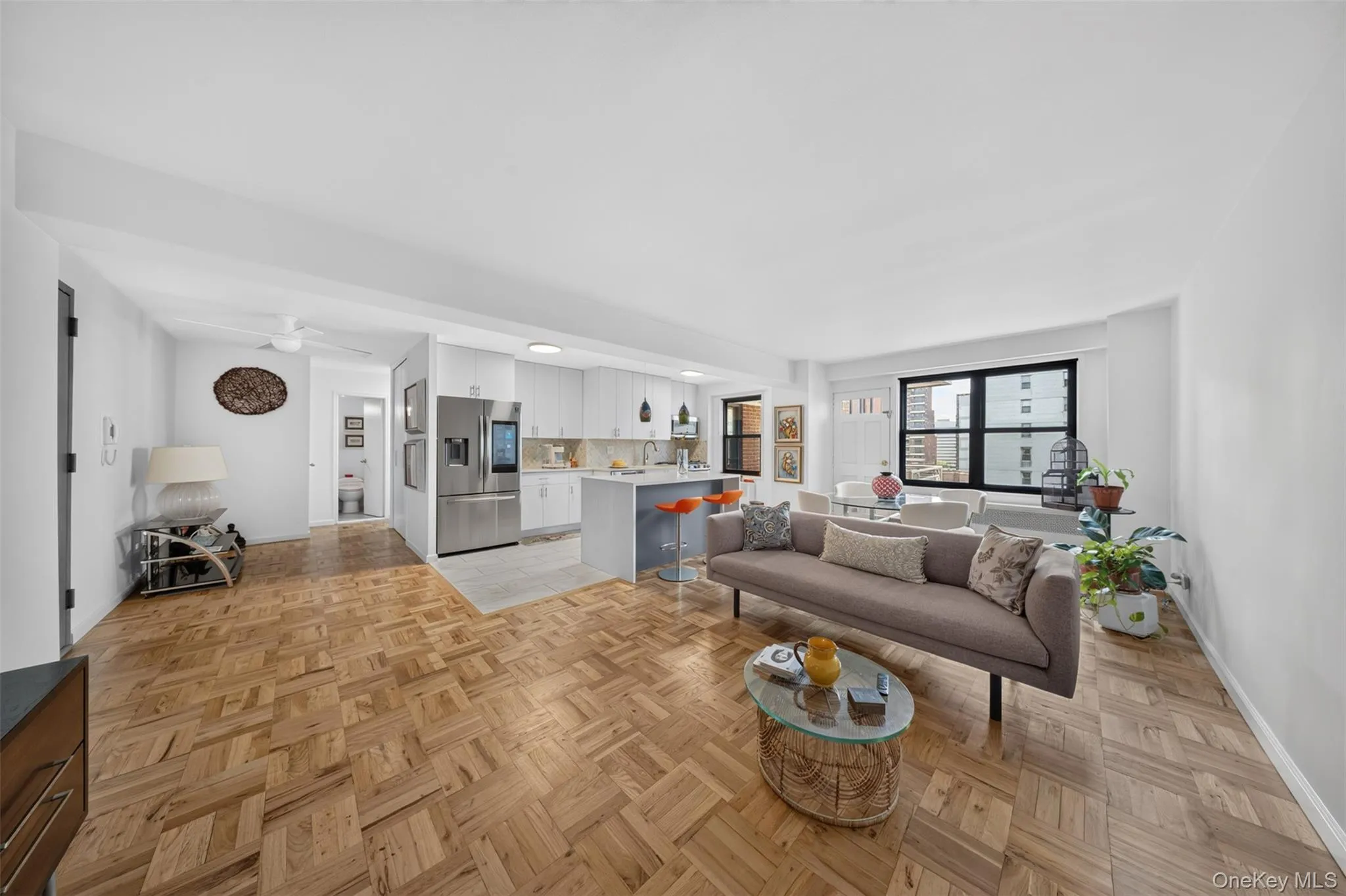 Open-concept living area with wood-finish flooring, a modern kitchen island, white cabinetry, and large windows Open-concept living area with wood-finish flooring, a modern kitchen island, white cabinetry, and large windows