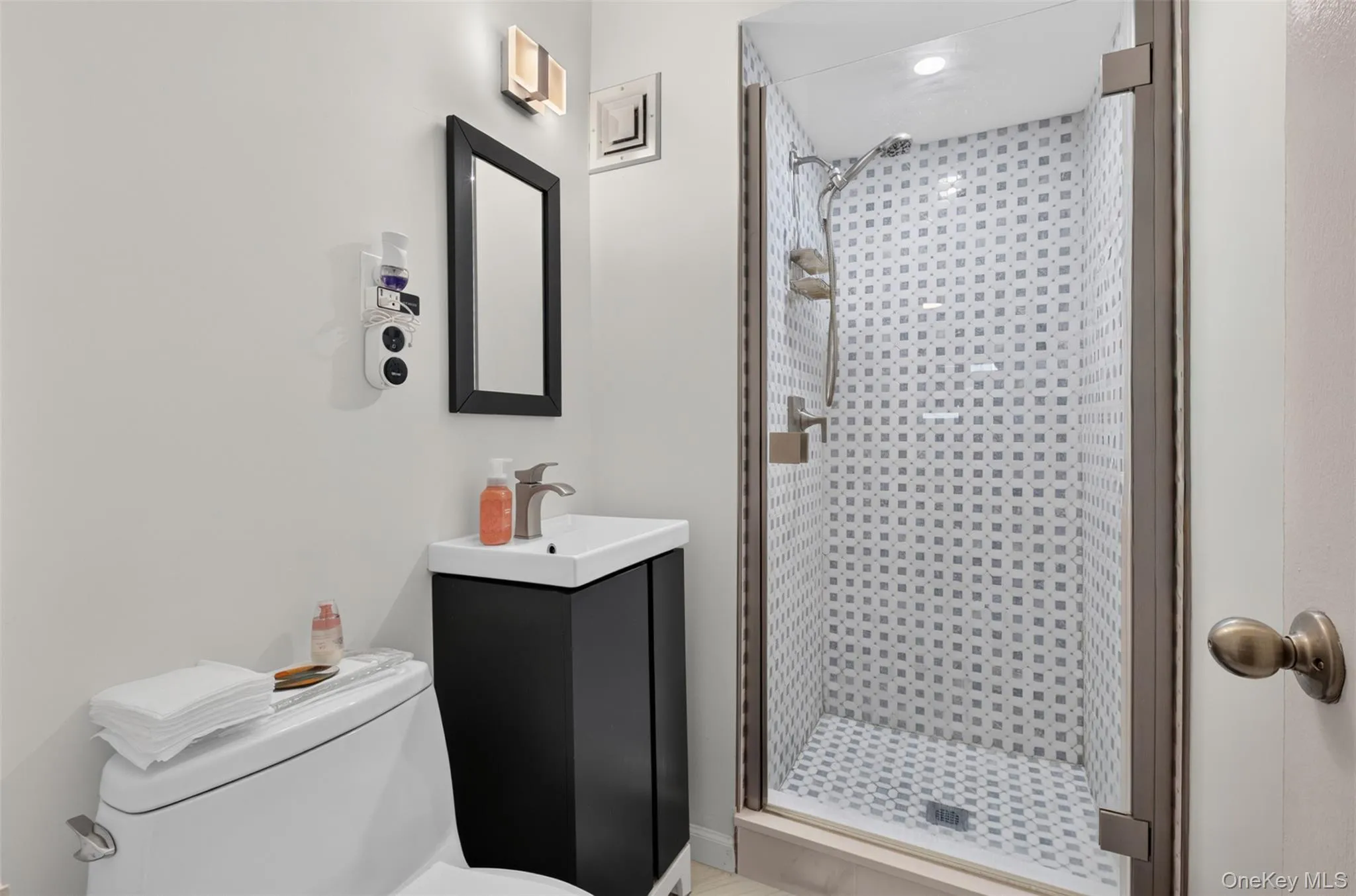 Glass-enclosed shower with mosaic tile surround, wall-mounted showerhead, and a rectangular floor drain Glass-enclosed shower with mosaic tile surround, wall-mounted showerhead, and a rectangular floor drain