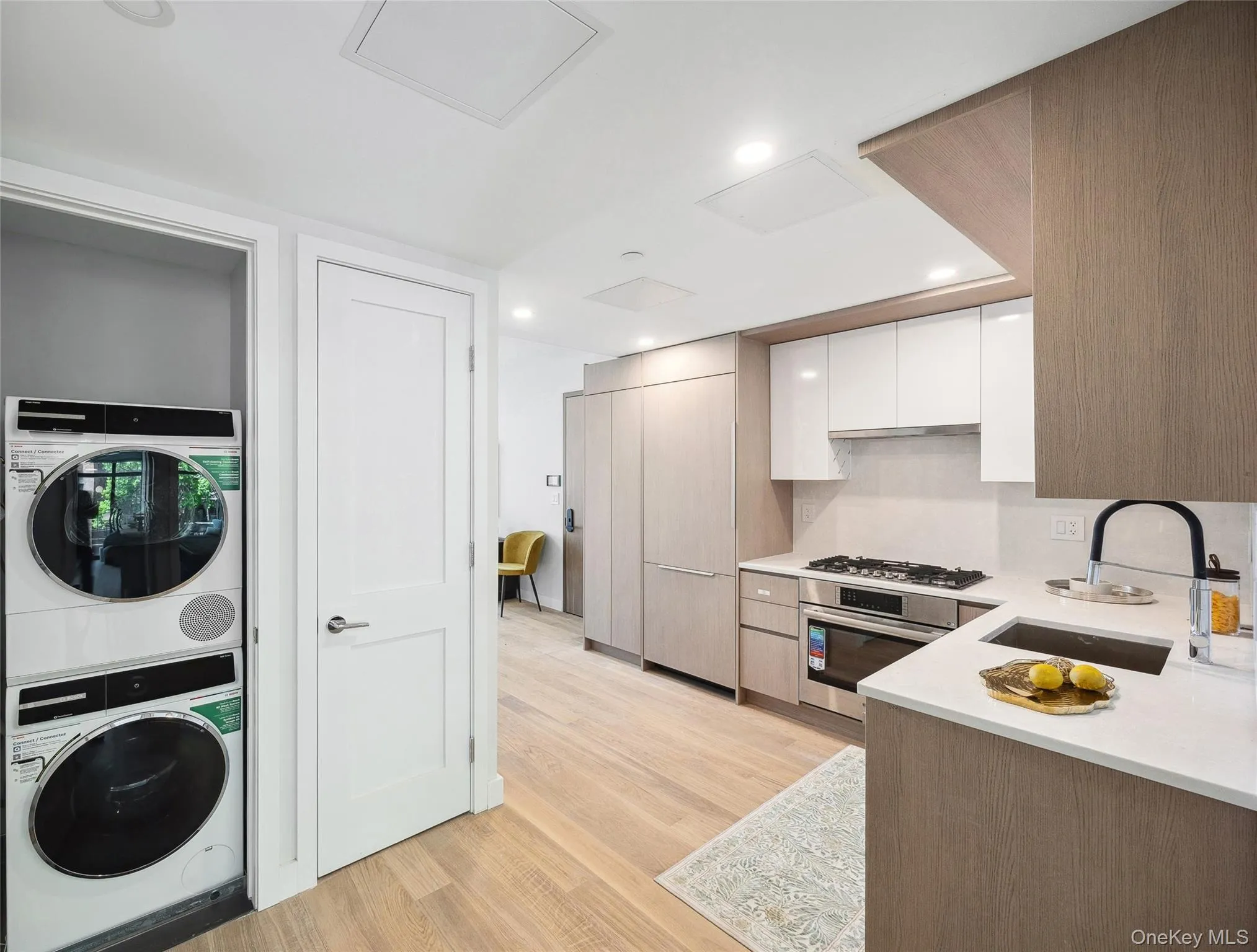 Kitchen featuring stainless steel appliances, a sink, stacked washer / drying machine, light countertops, and white cabinets Kitchen featuring stainless steel appliances, a sink, stacked washer / drying machine, light countertops, and white cabinets