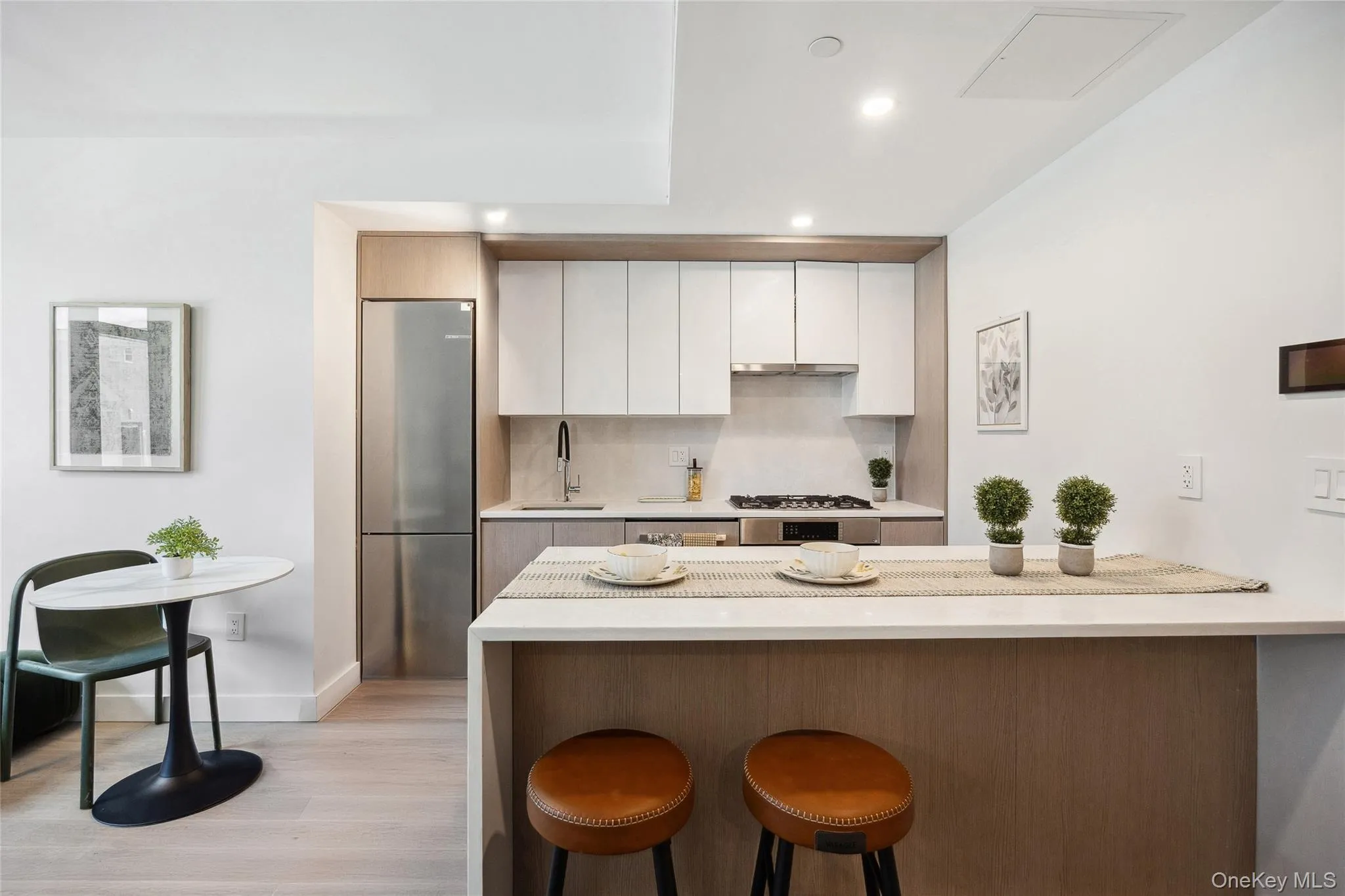 Kitchen with freestanding refrigerator, a breakfast bar area, a sink, white cabinetry, and light wood-style floors Kitchen with freestanding refrigerator, a breakfast bar area, a sink, white cabinetry, and light wood-style floors