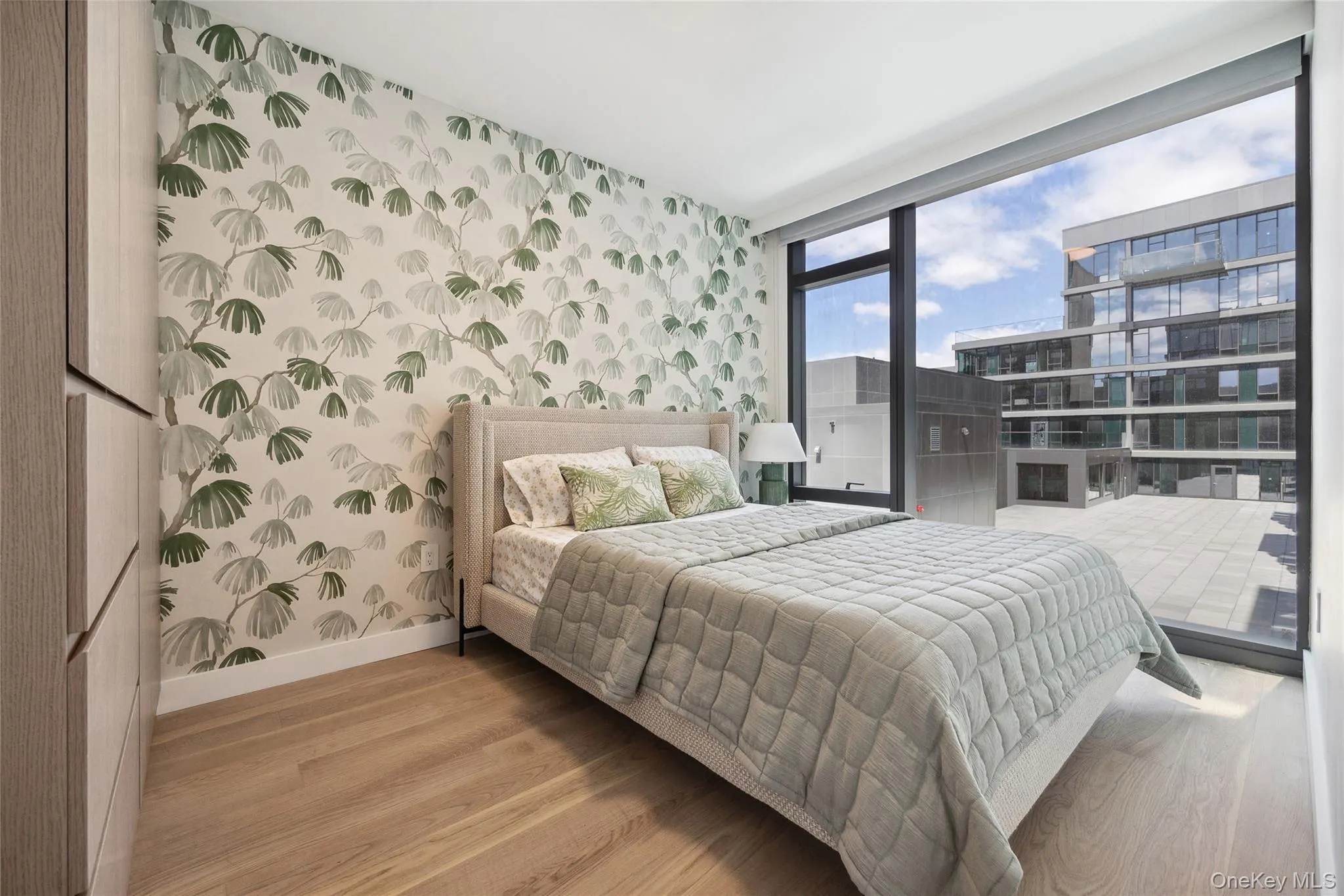 Bedroom featuring wallpapered walls, baseboards, wood finished floors, an accent wall, and a wall of windows Bedroom featuring wallpapered walls, baseboards, wood finished floors, an accent wall, and a wall of windows