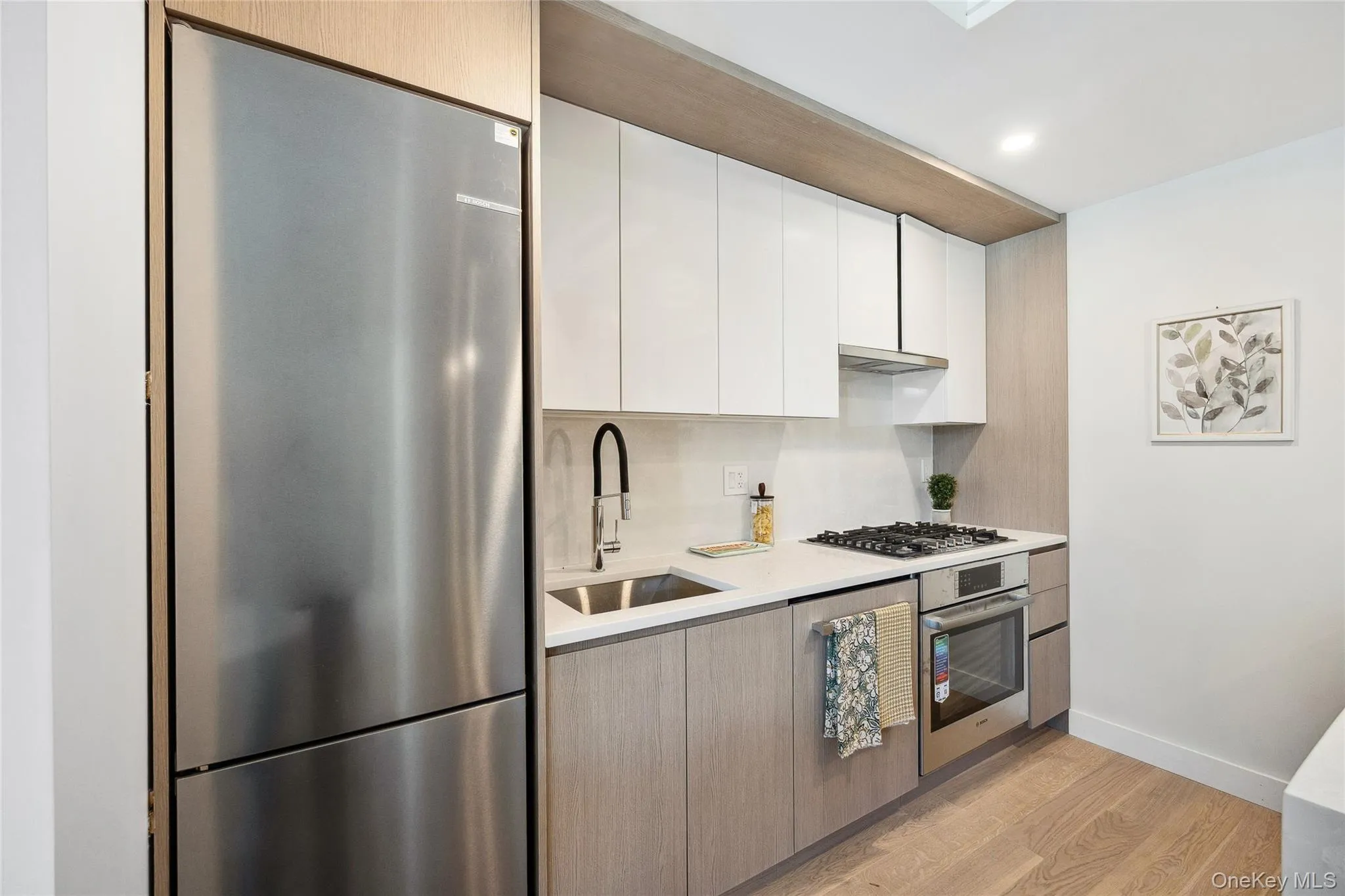Kitchen with appliances with stainless steel finishes, a sink, light countertops, light wood-style flooring, and white cabinetry Kitchen with appliances with stainless steel finishes, a sink, light countertops, light wood-style flooring, and white cabinetry