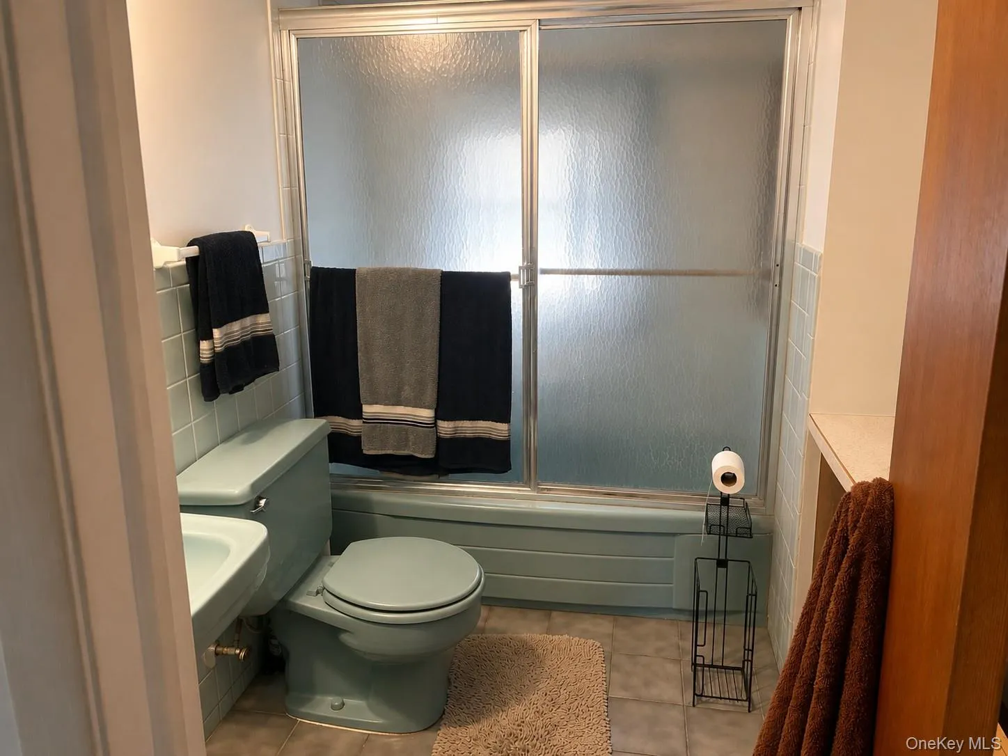 Bathroom featuring a tiled floor, blue-hued tub surround, a shower with sliding frosted glass doors, and light blue fixtures Bathroom featuring a tiled floor, blue-hued tub surround, a shower with sliding frosted glass doors, and light blue fixtures