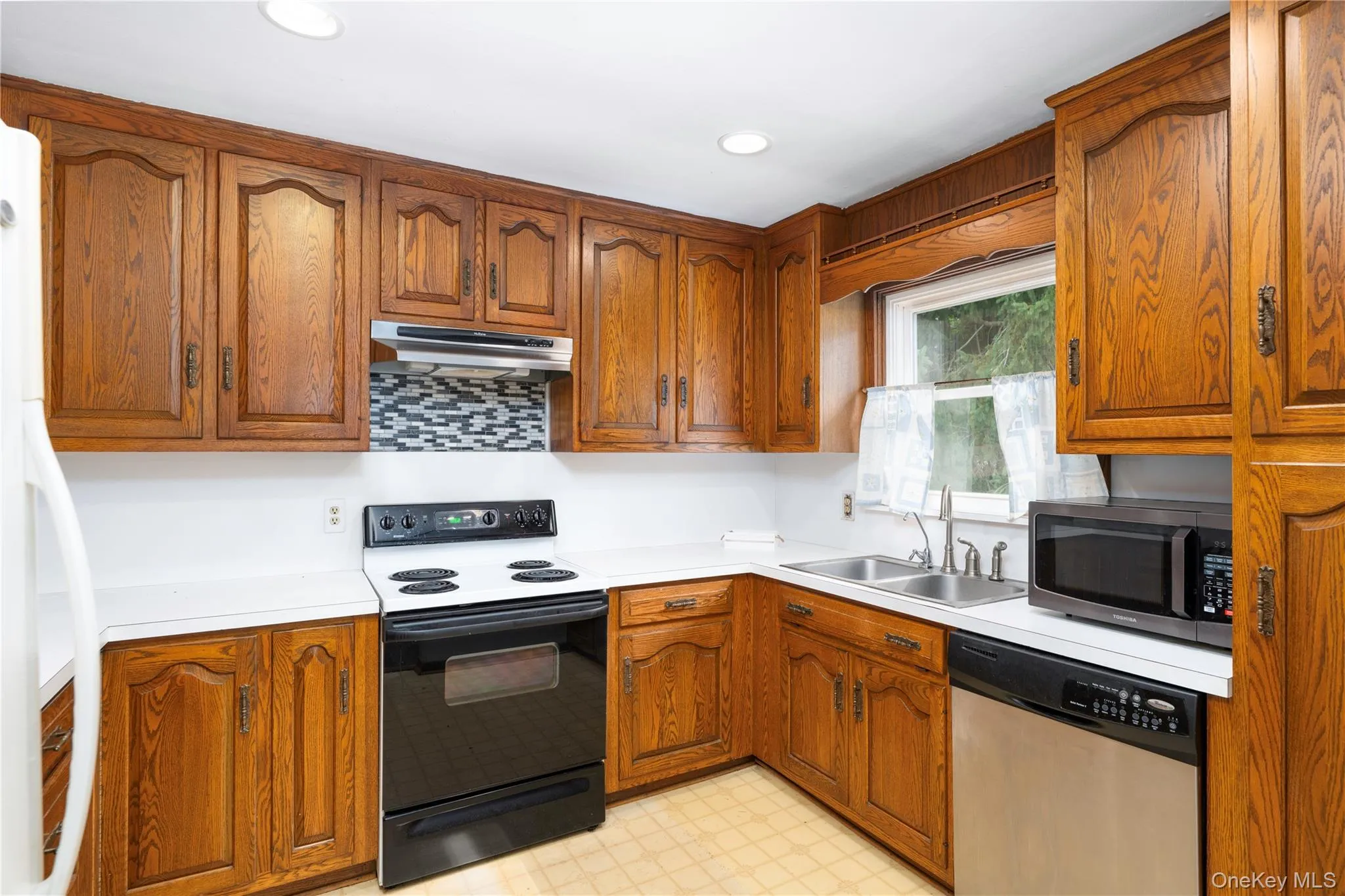 Wood cabinetry with dark hardware, white countertops, stainless steel sink, black range, and stainless steel dishwasher Wood cabinetry with dark hardware, white countertops, stainless steel sink, black range, and stainless steel dishwasher