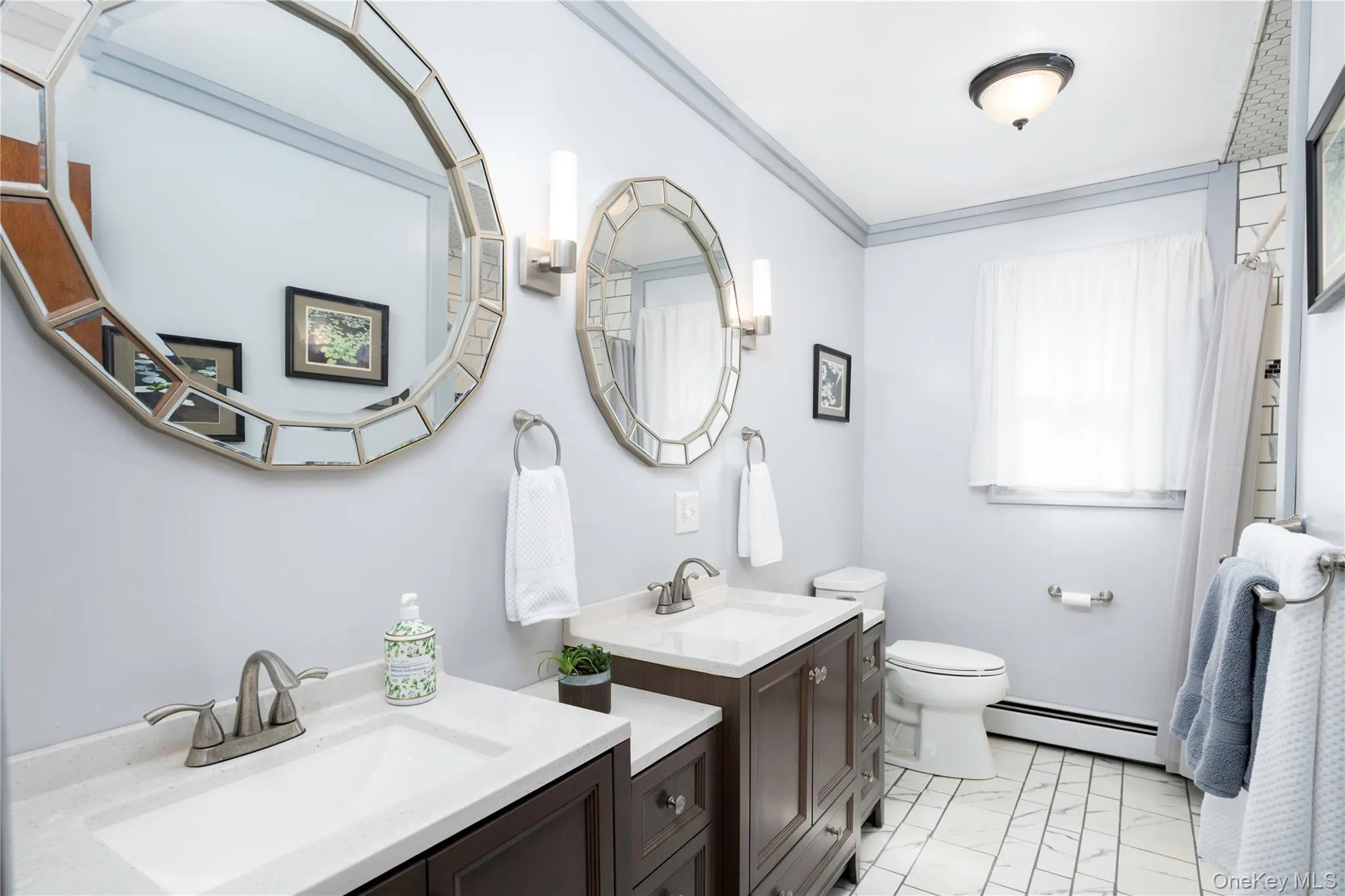 Dual vanities with white countertops, decorative framed mirrors, brushed nickel hardware, and tile flooring Dual vanities with white countertops, decorative framed mirrors, brushed nickel hardware, and tile flooring